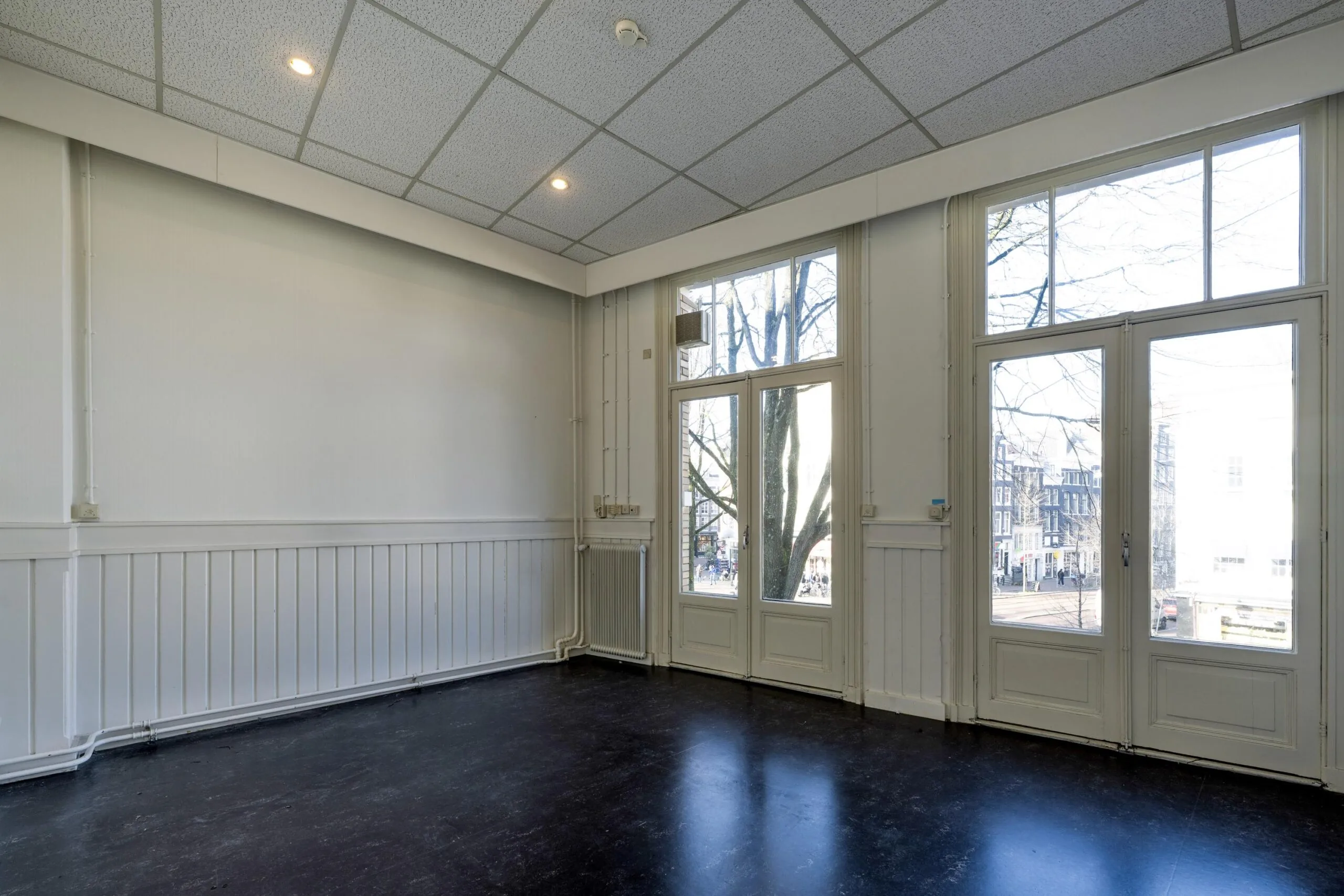 Een lege kamer met grote ramen en uitzicht op de straat.