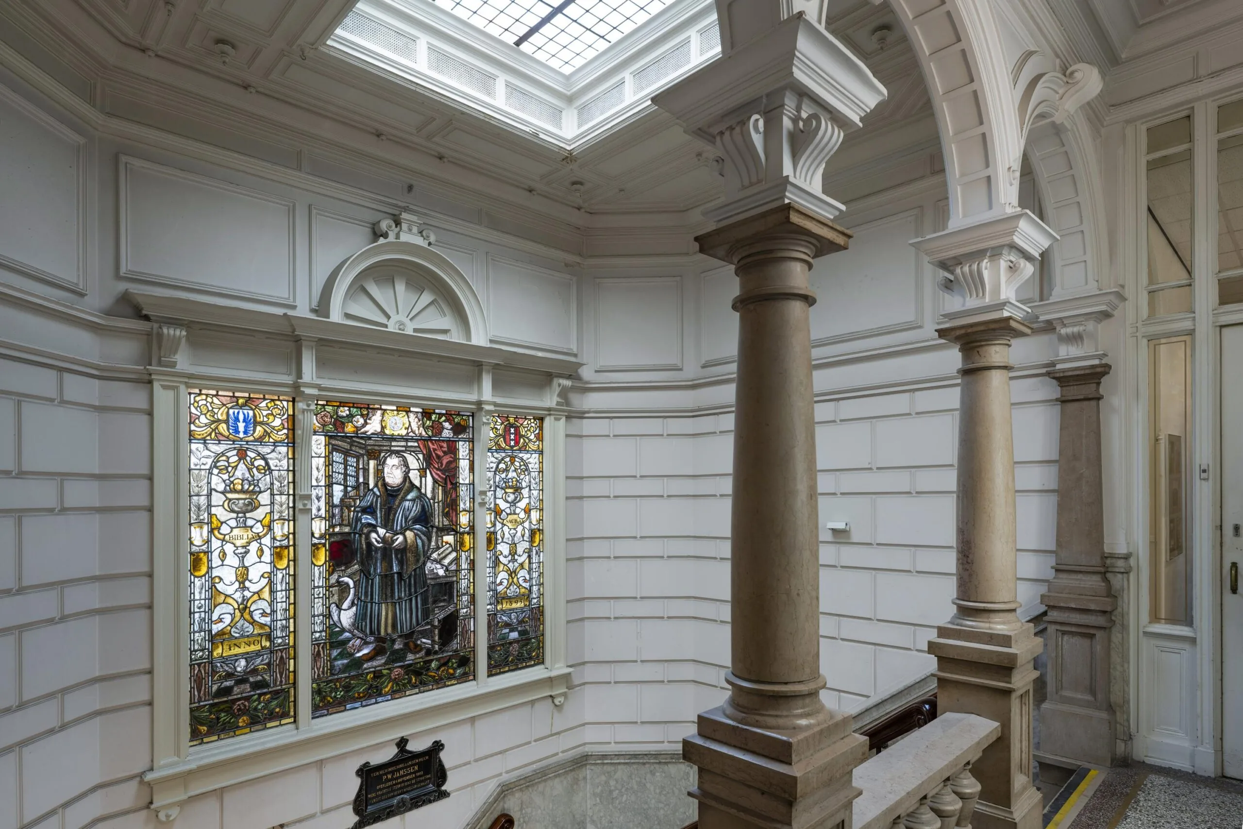 Interieur van een gebouw met glas-in-loodraam en decoratieve zuilen.
