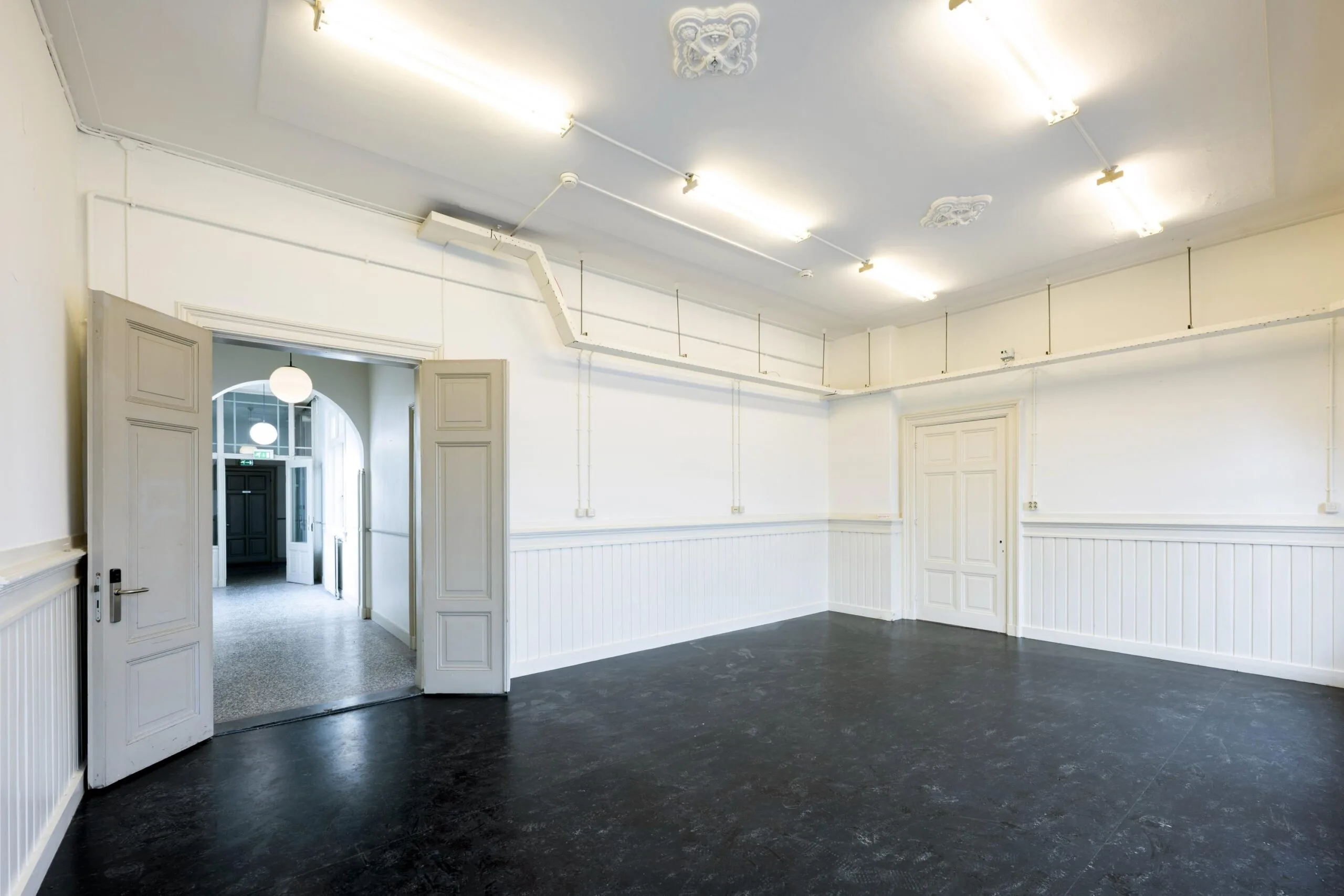 Lege kamer met witte muren en een openstaande dubbele deur die naar een gang leidt.