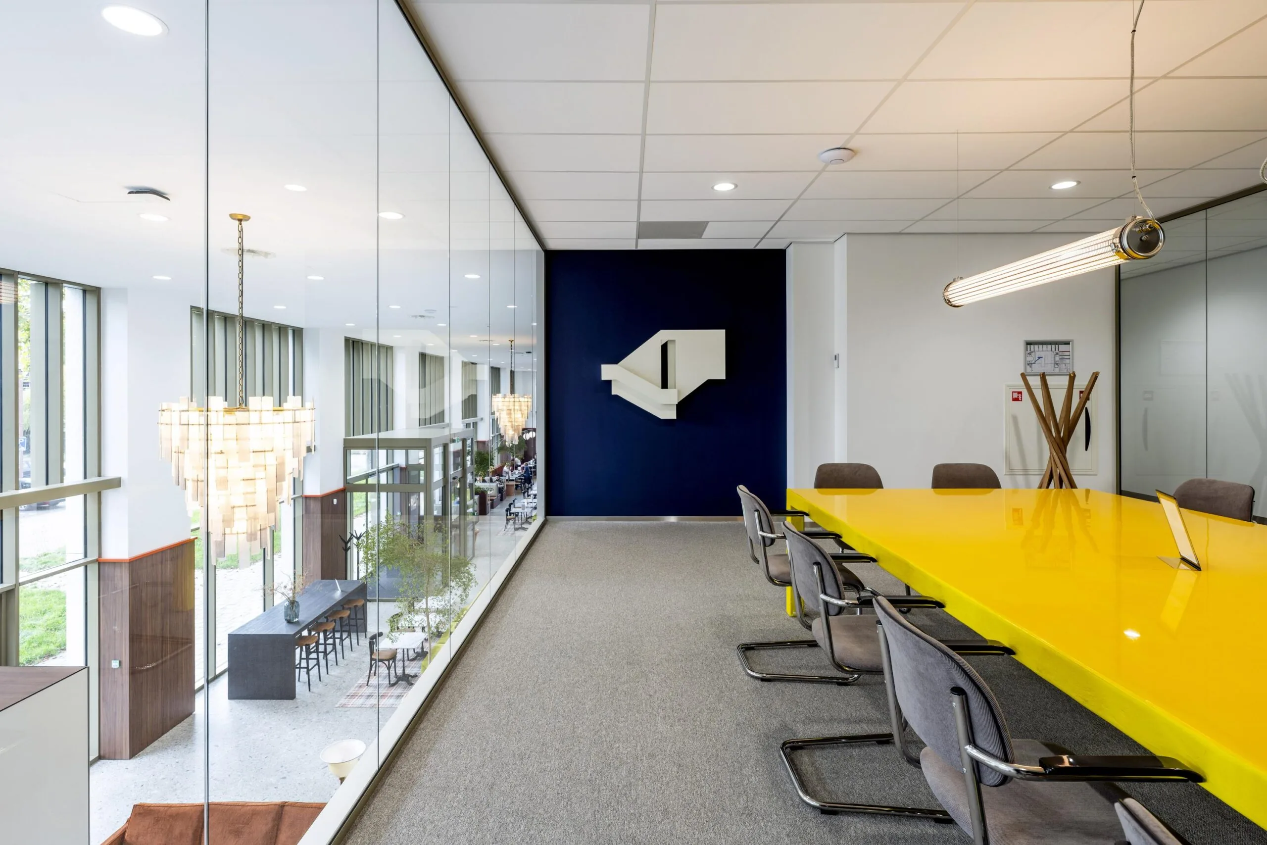 Vergaderruimte met een lange gele tafel en een moderne glazen wand aan de Willem Fenengastraat.