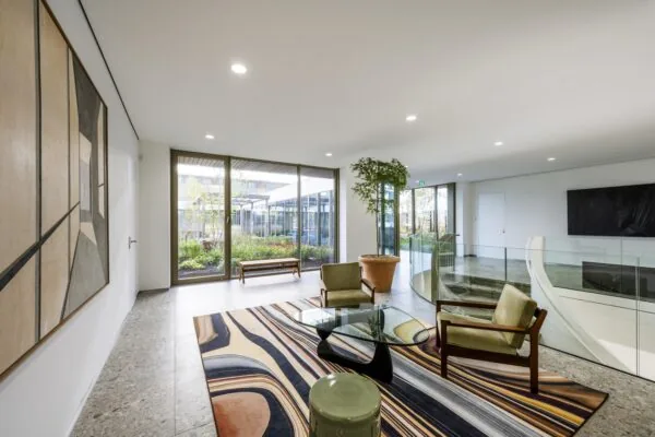 Een moderne, lichte lobby met kunst, een kleurrijk vloerkleed en grote ramen met uitzicht op een tuin.