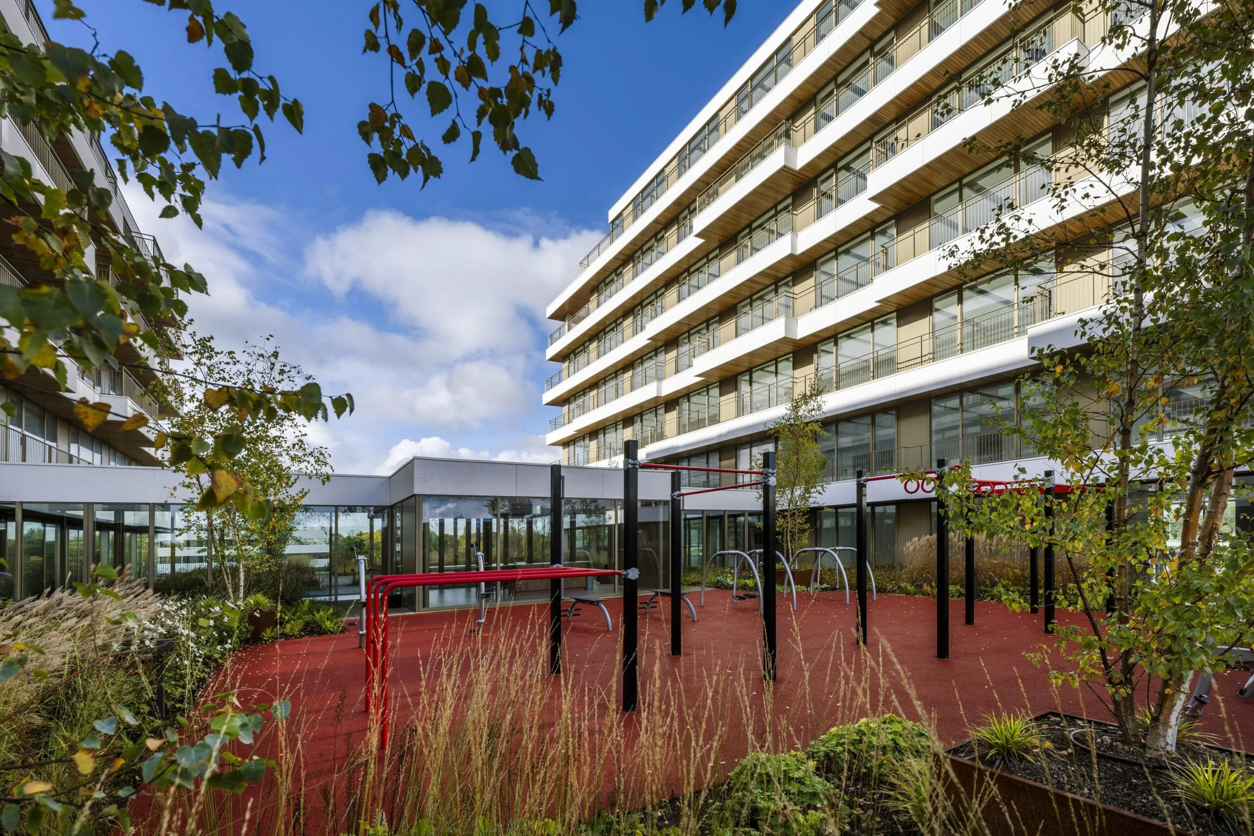 Een modern gebouw met speeltoestellen op een buitenplein omgeven door groen.