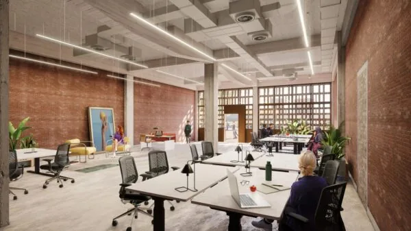 Een moderne kantoorruimte met open indeling, bakstenen muren en grote ramen, waar mensen aan bureaus werken.