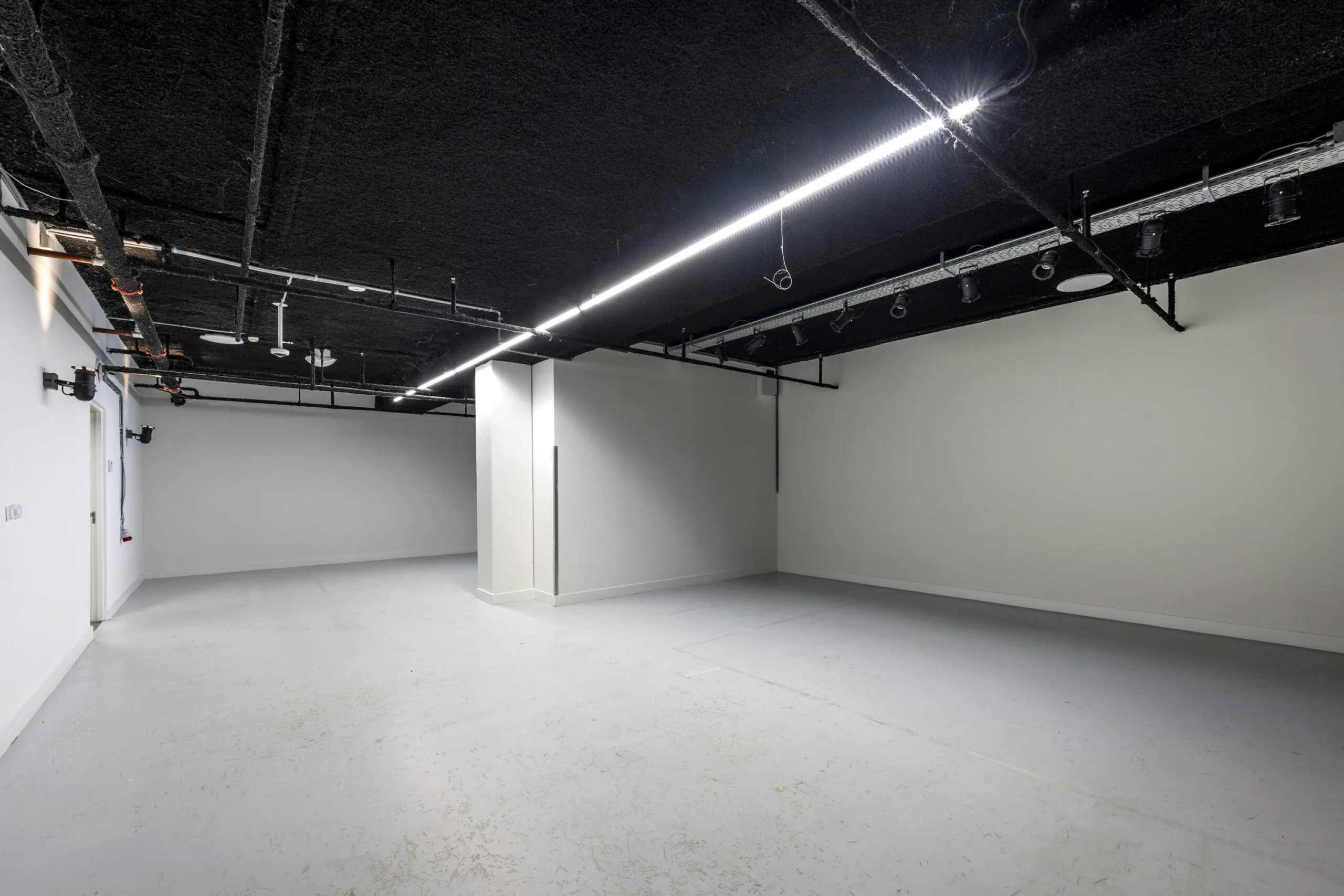 Een lege, industriële ruimte met donker plafond en strakke verlichting aan de Roetersstraat.