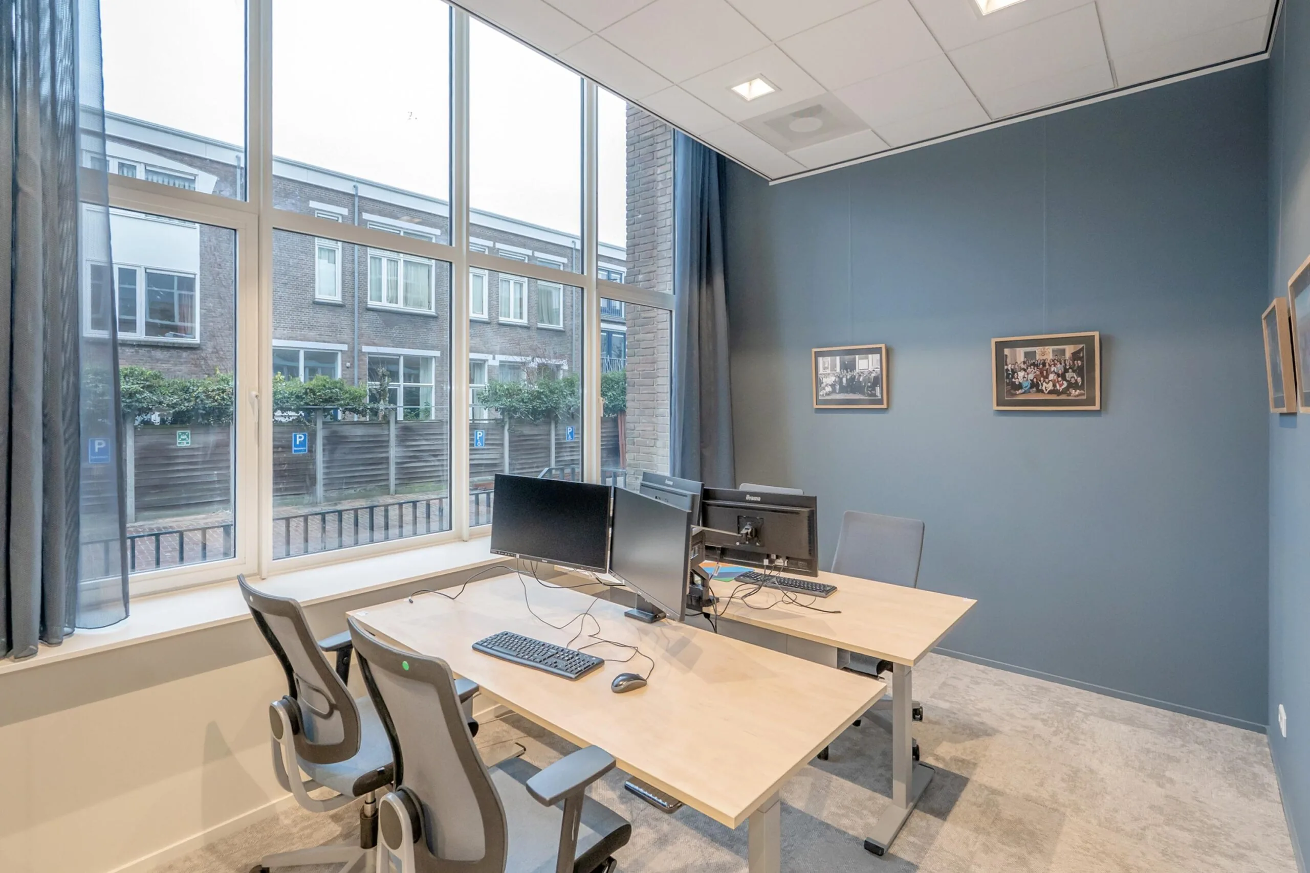Een moderne kantoorruimte met bureaus, stoelen en computerschermen, met zicht op een gebouw buiten het raam.