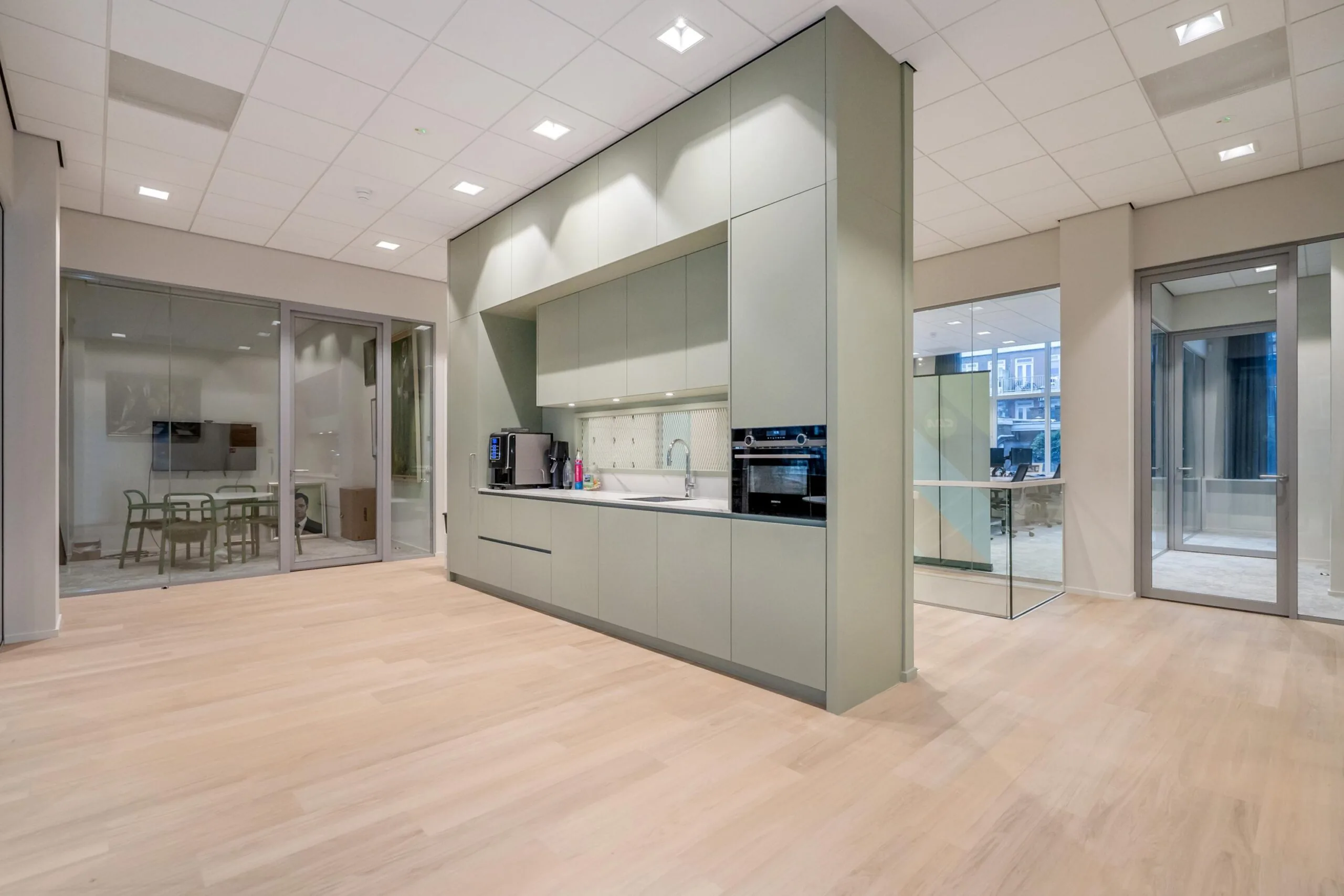 Een moderne keuken in een kantooromgeving met glazen wanden en houten vloeren.