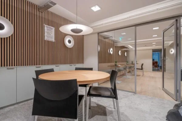 Een moderne vergaderruimte met een ronde houten tafel, zwarte stoelen en houten lambrisering op de muur.