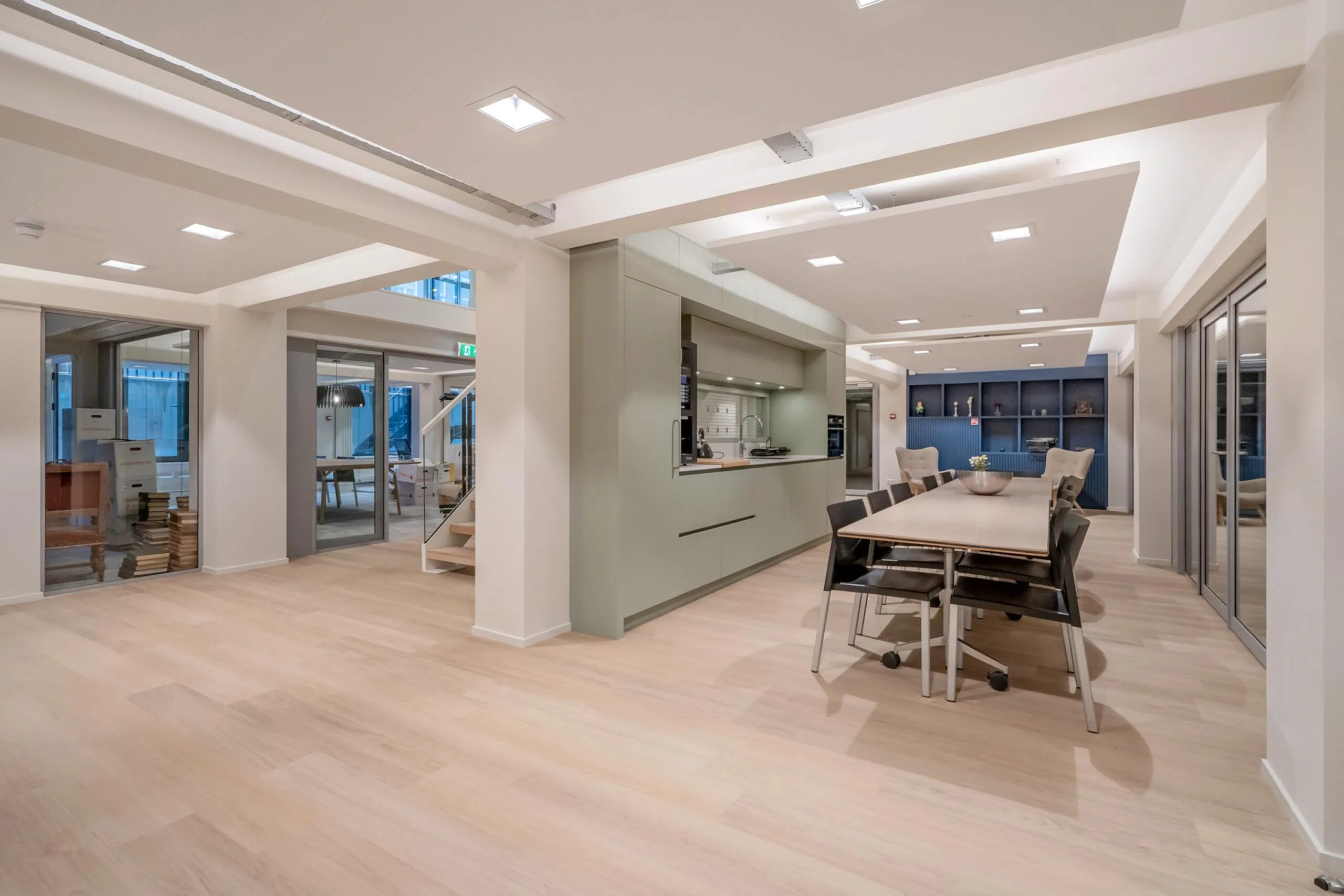 Een modern, ruim interieur van een kantoor met houten vloer, vergadertafel en open keuken.