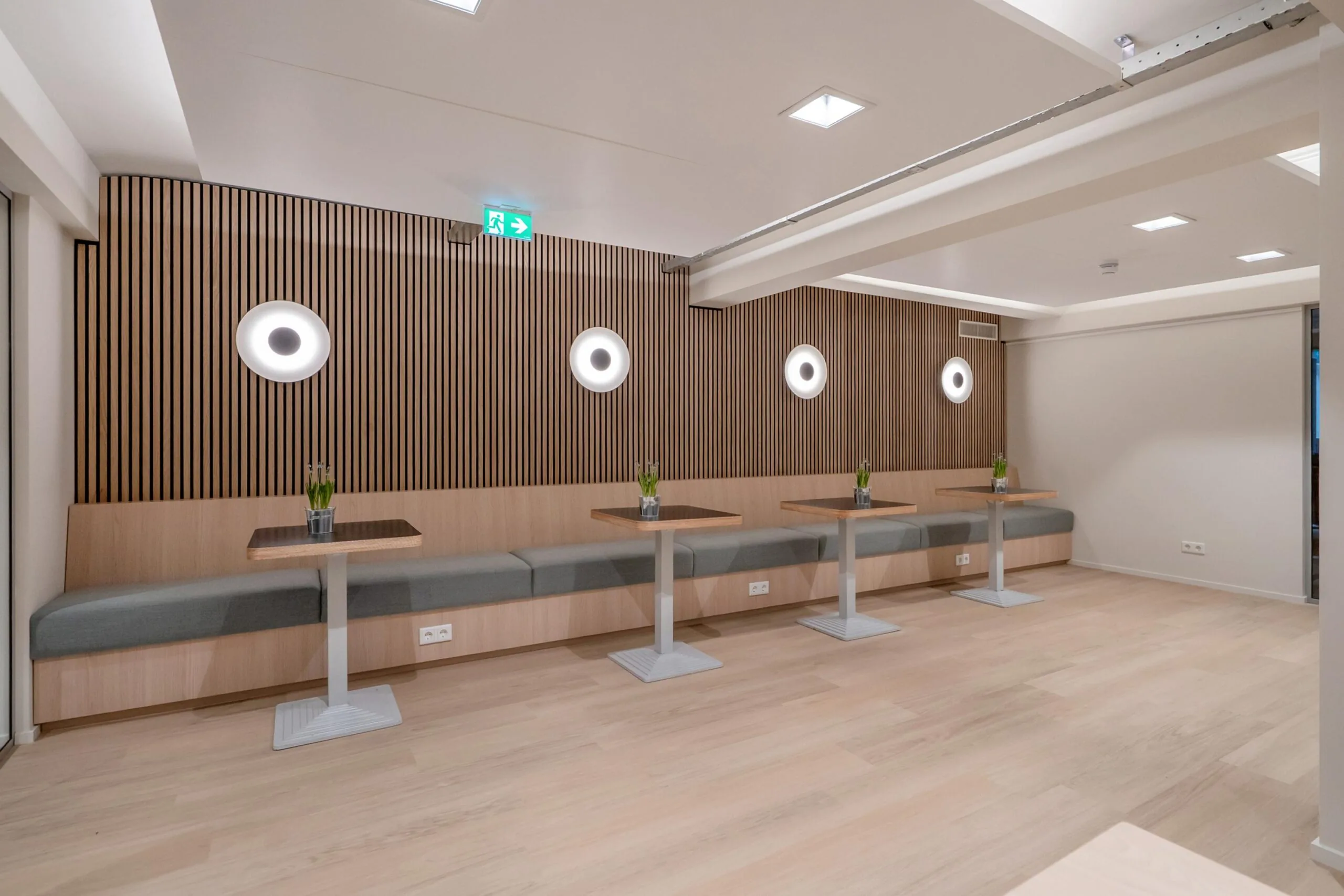 Een moderne zitruimte met houten wanden, grijze banken en tafels met planten in potten.