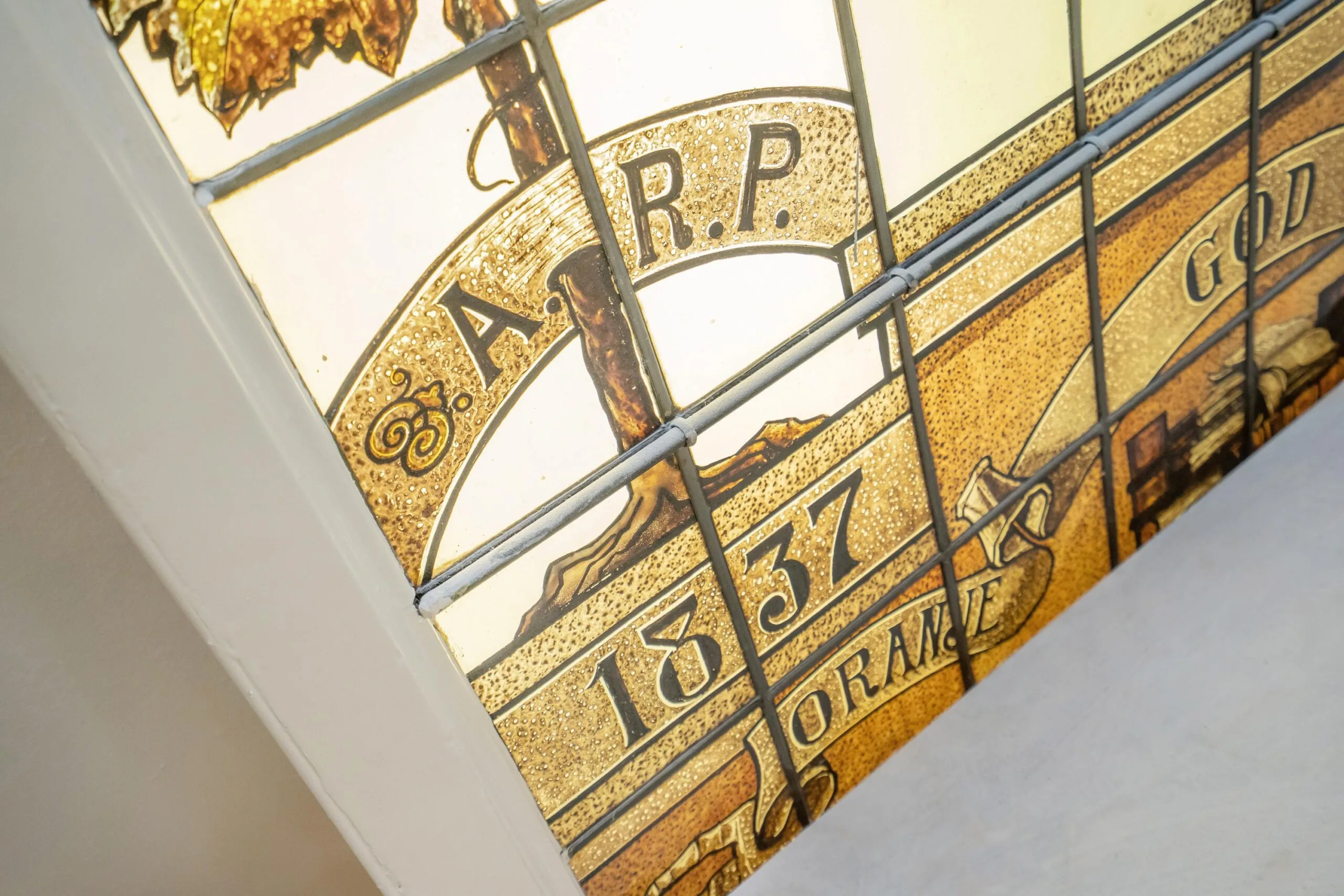 Glas-in-loodraam met de inscriptie "A.R.P." en "1837", met decoratieve elementen en teksten.