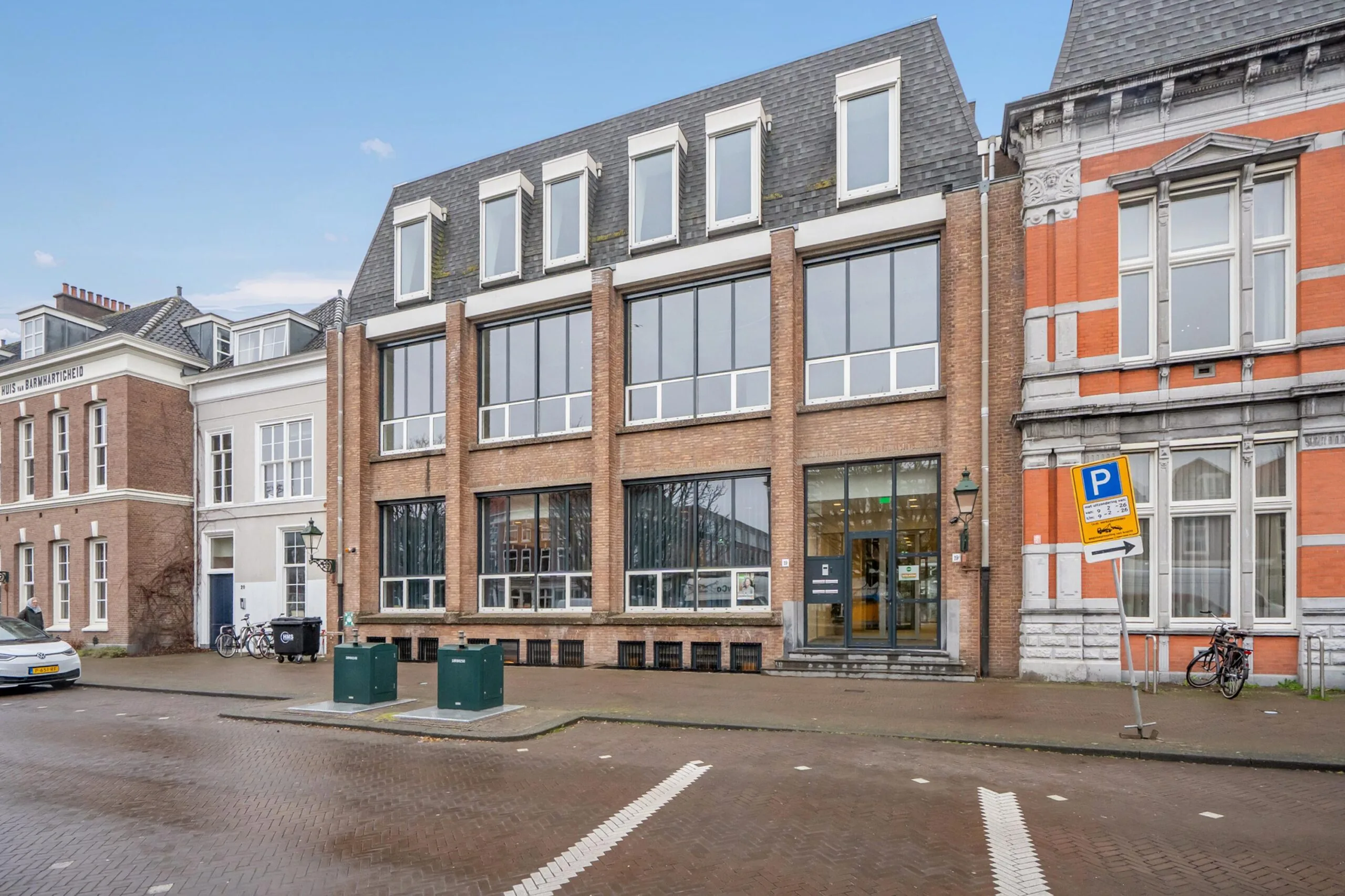Een moderne bakstenen kantoorgebouw met grote ramen naast historische panden.