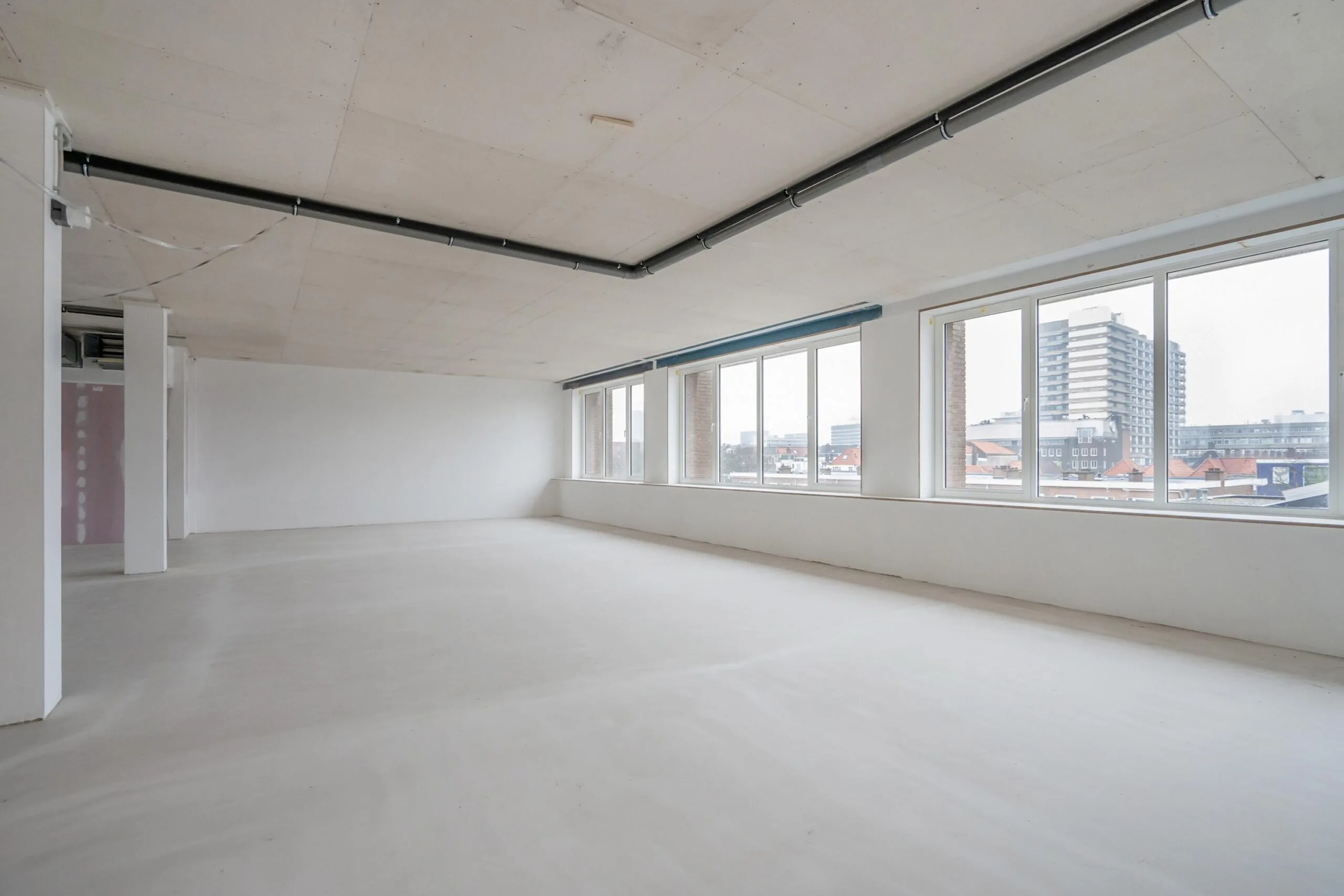 Lege, lichte kantoorruimte met grote ramen en uitzicht op moderne gebouwen.