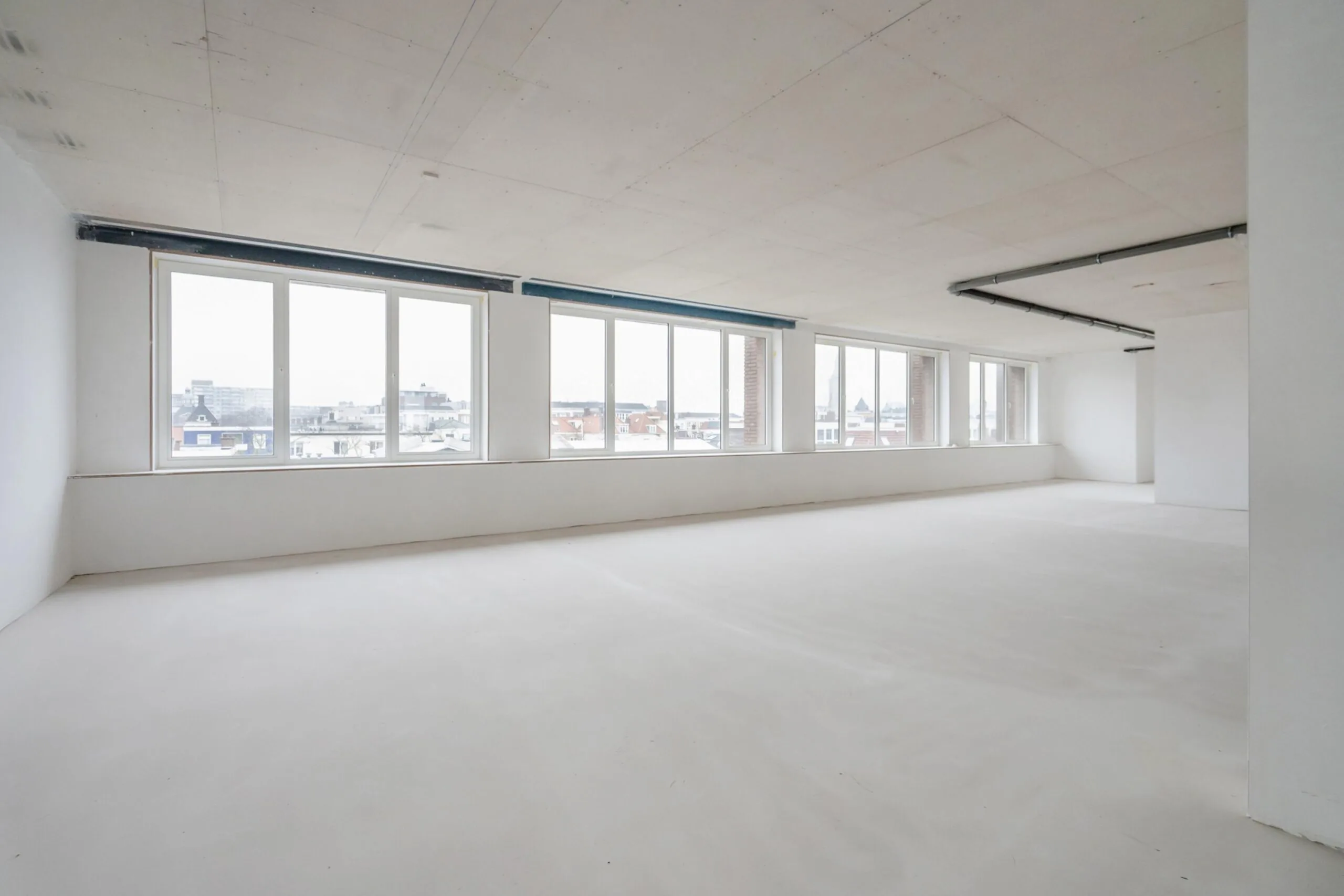 Een leeg, licht open kantoor met grote ramen en uitzicht over de stad.