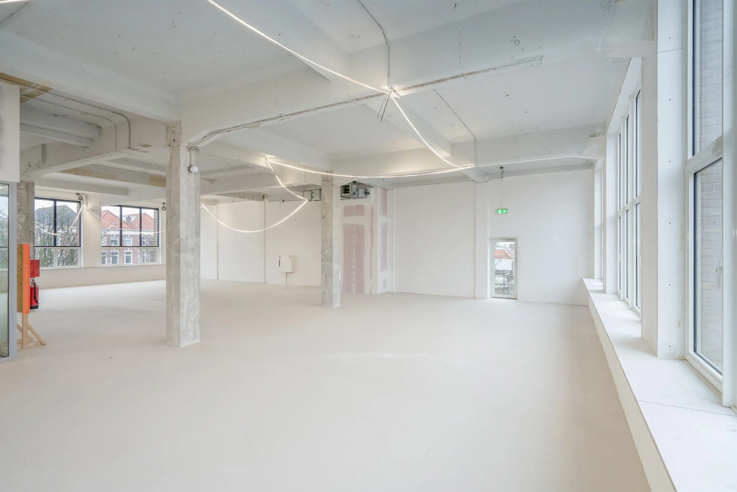 Een lege, ruime, lichte kamer met grote ramen en een industriële uitstraling.