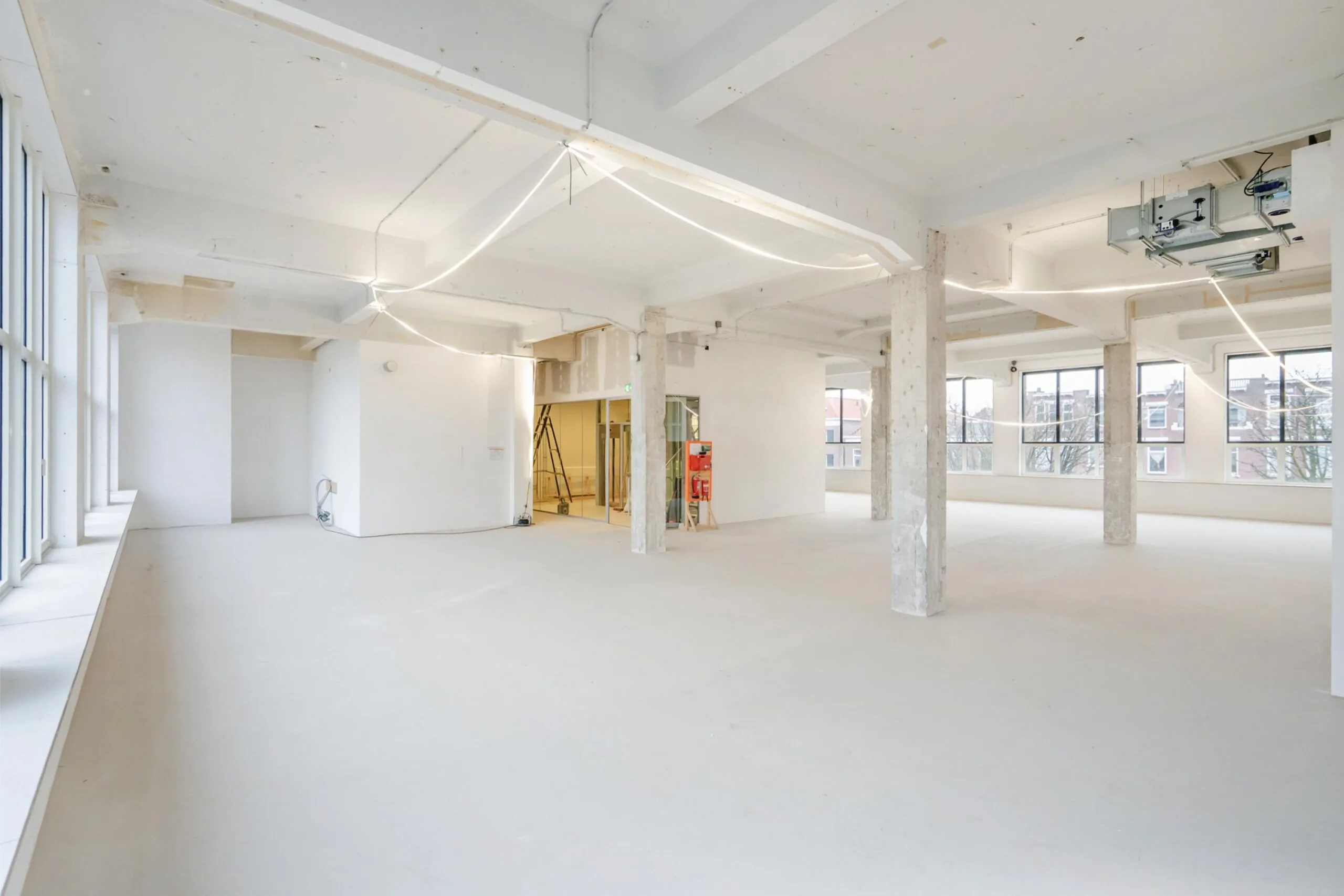 Een ruime, lichte, lege kantoorruimte met grote ramen en zicht op een stedelijk landschap.