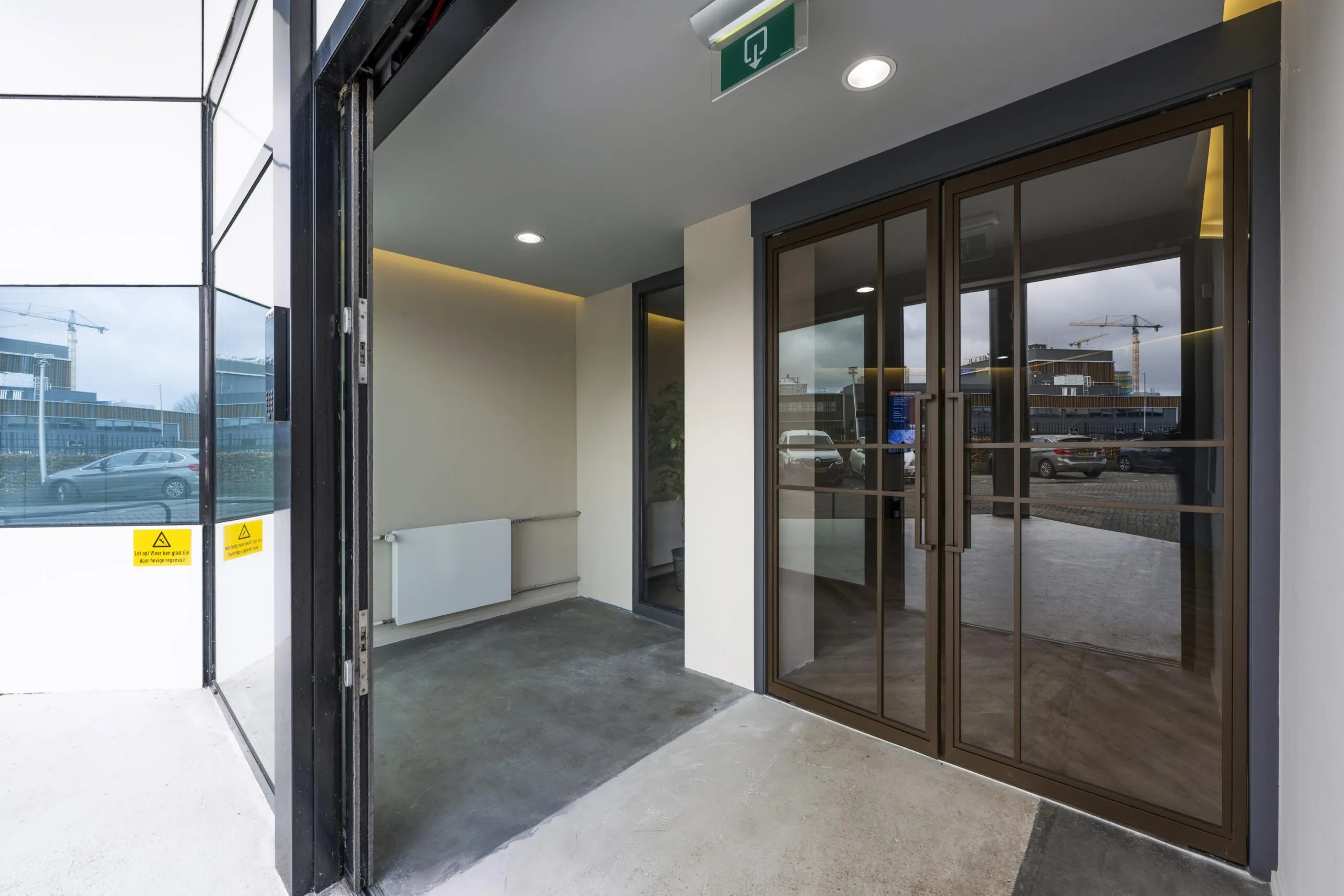 Ingang van een modern bedrijfsgebouw aan de Kuiperbergweg met glazen deuren en zicht op een parkeerplaats.