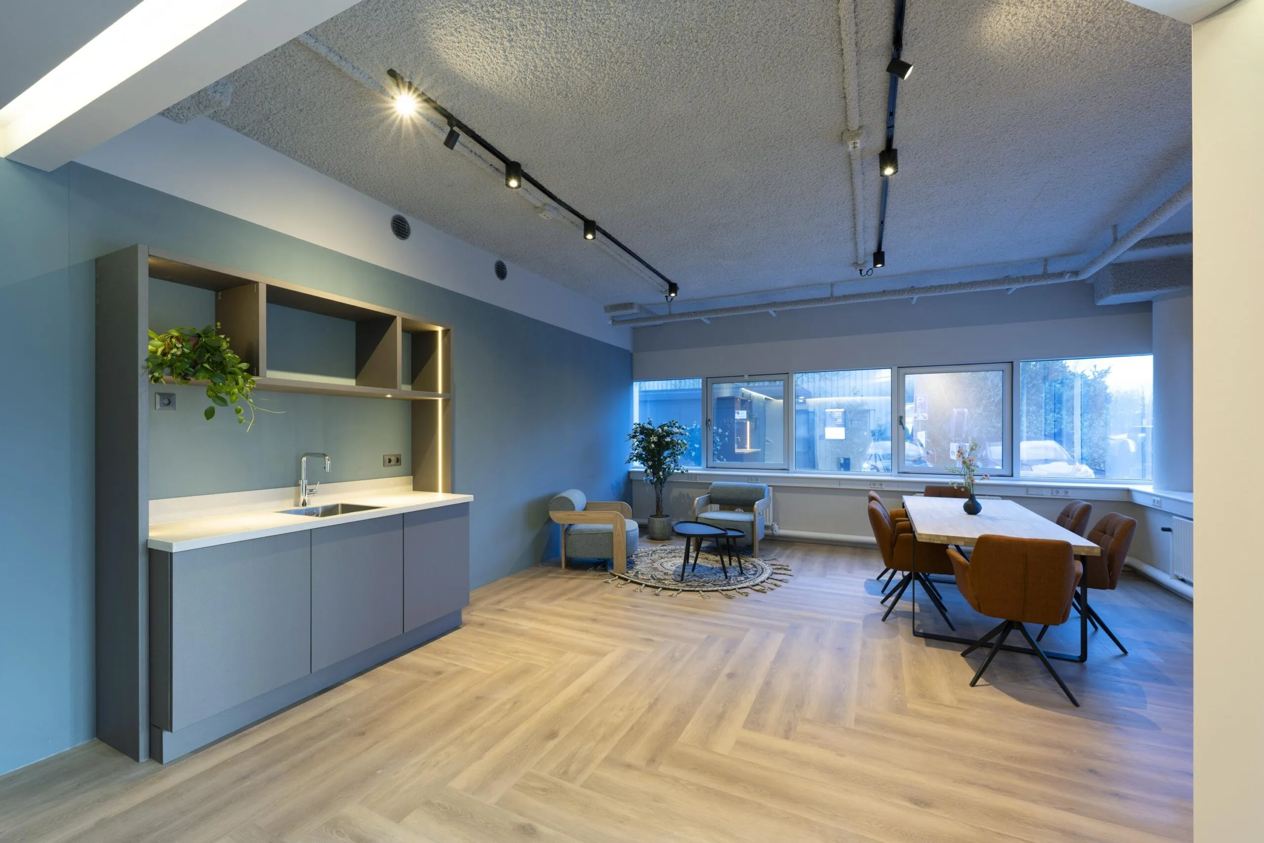Moderne kantoorruimte met keukenblok, vergadertafel en zithoek.