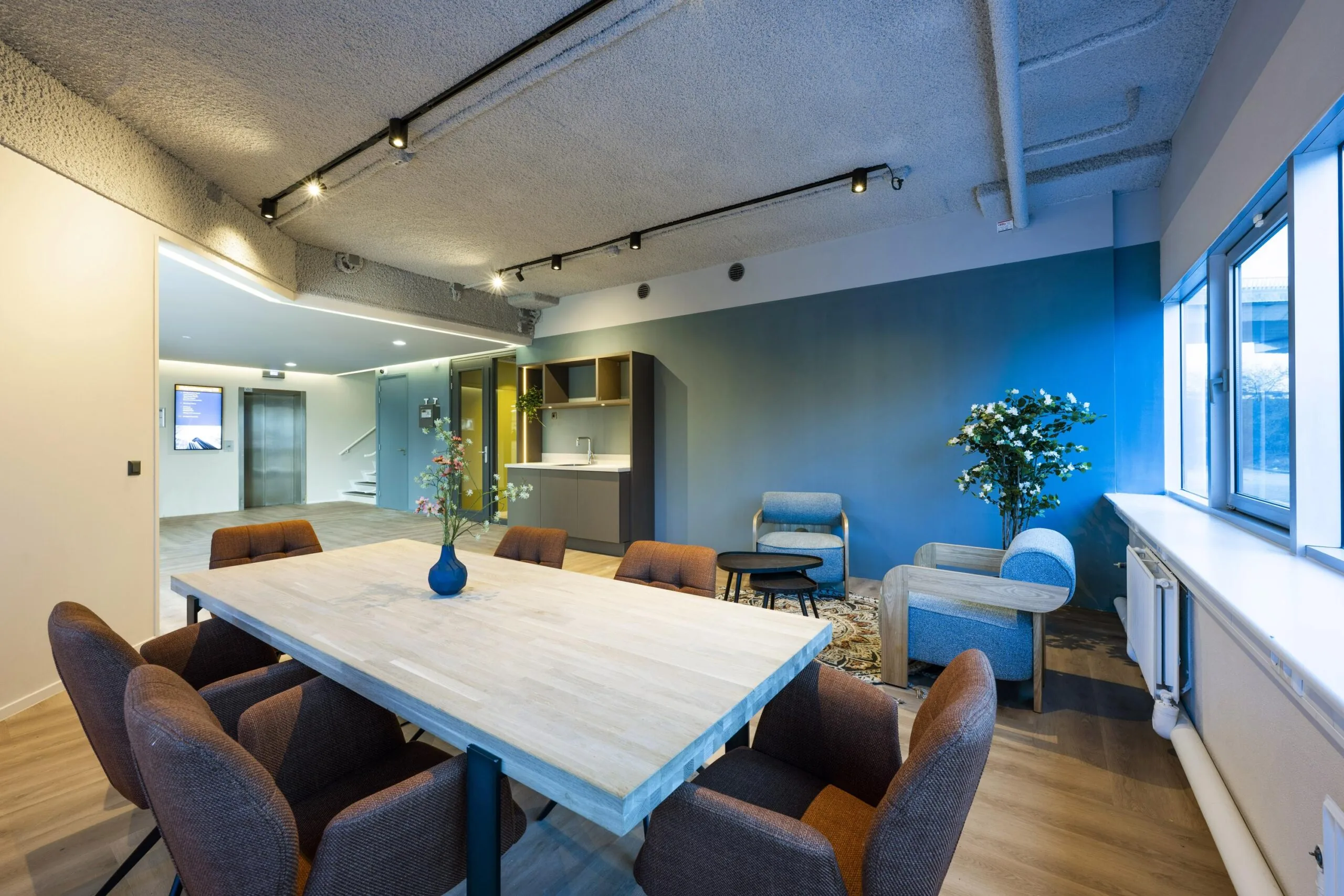 Moderne vergaderruimte met houten tafel, comfortabele stoelen, en een zithoek met planten.