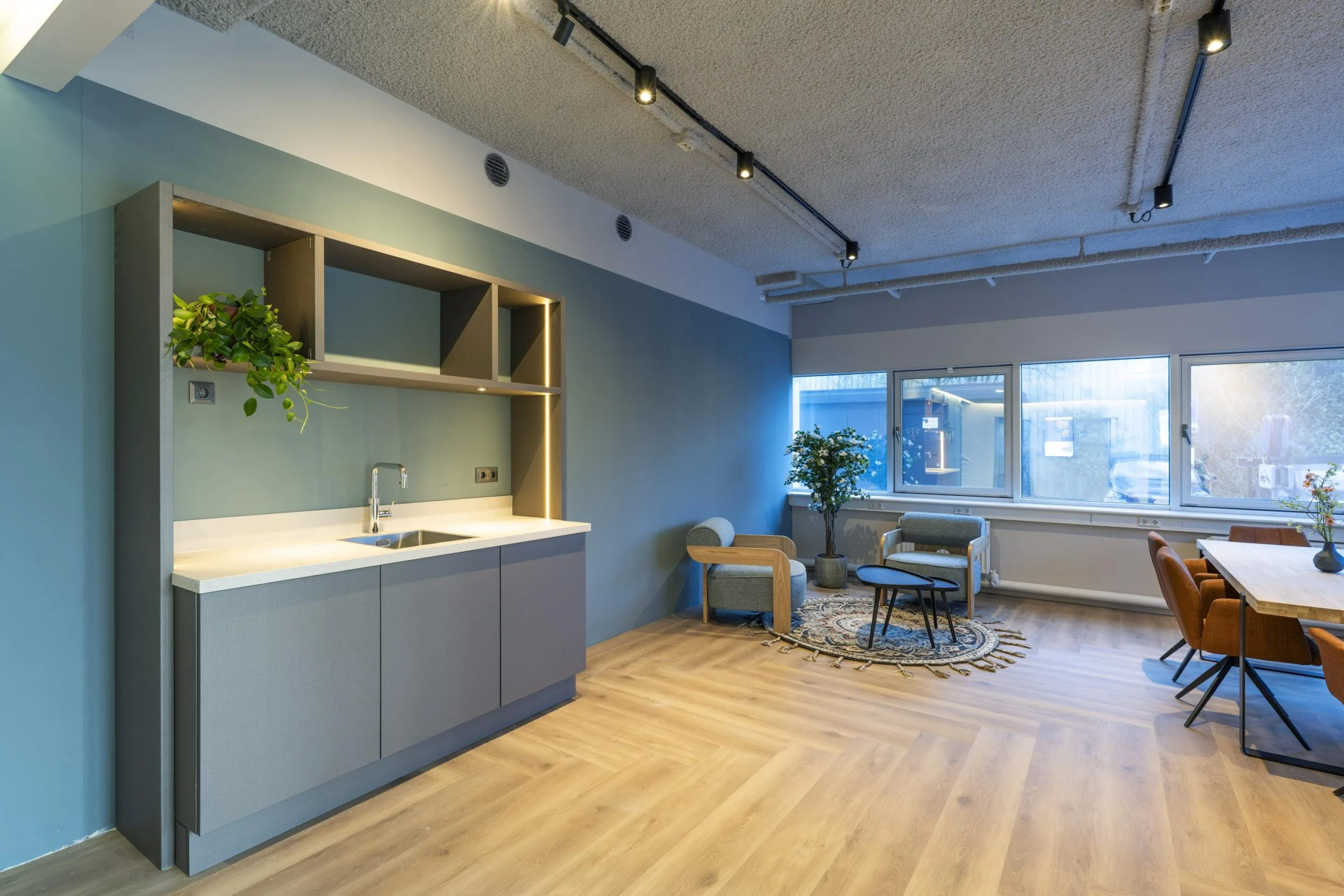 Een moderne kantoorruimte met een kitchenette, zitgedeelte en grote ramen.