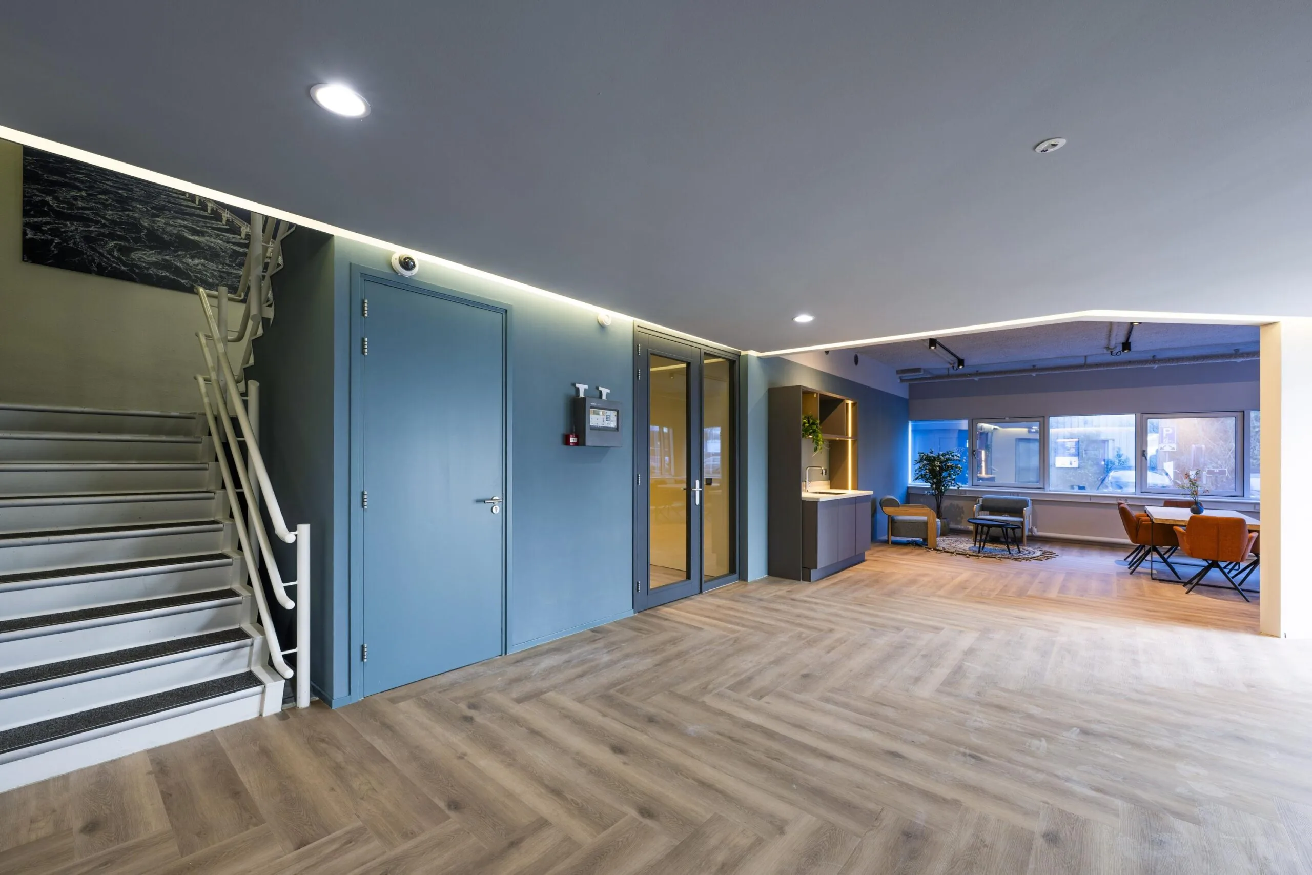 Een modern interieur met een trap, blauwe deuren, en een zithoek met een tafel en stoelen.