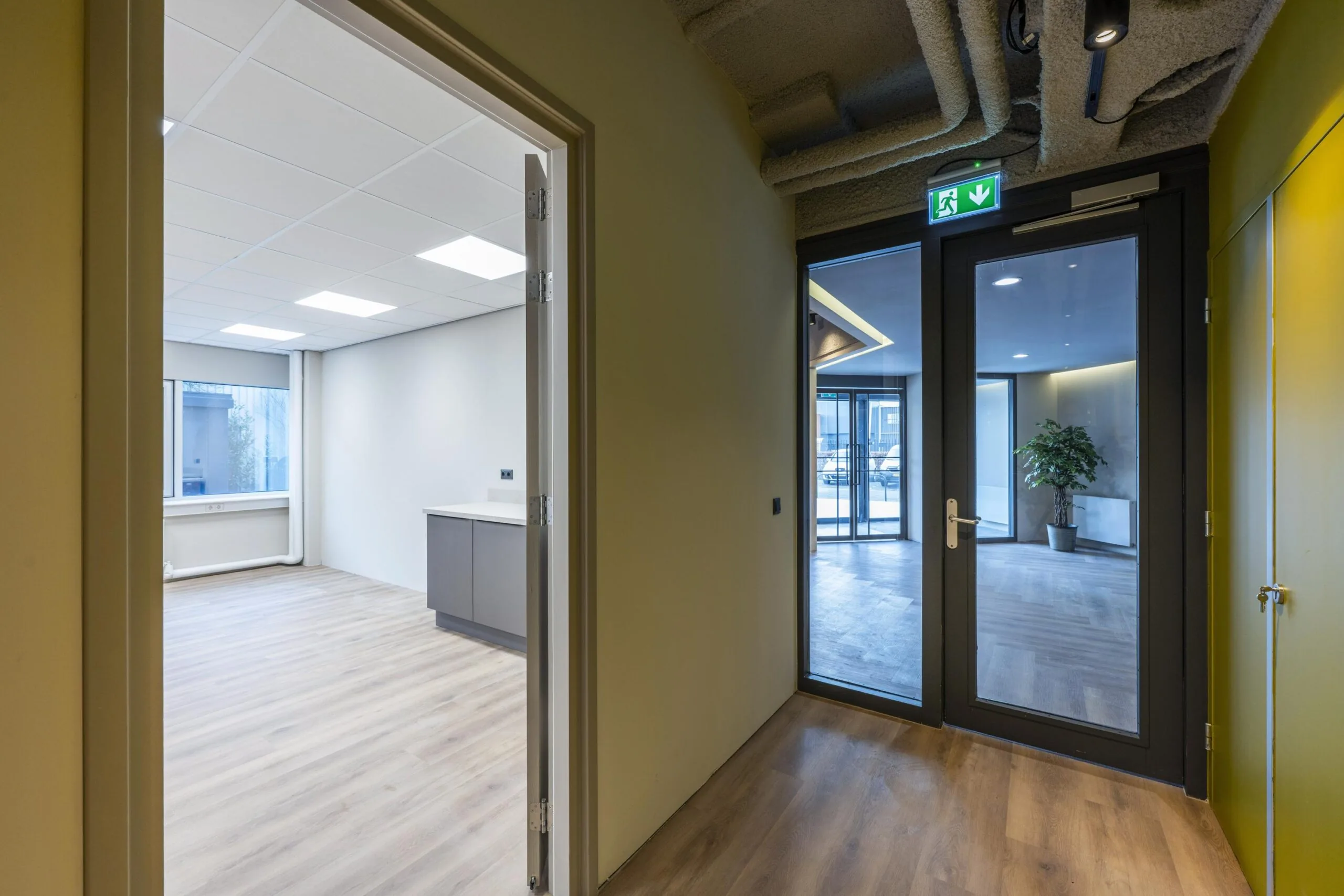 Een lege kantoorruimte met houten vloer en een glazen deur naar de gang.