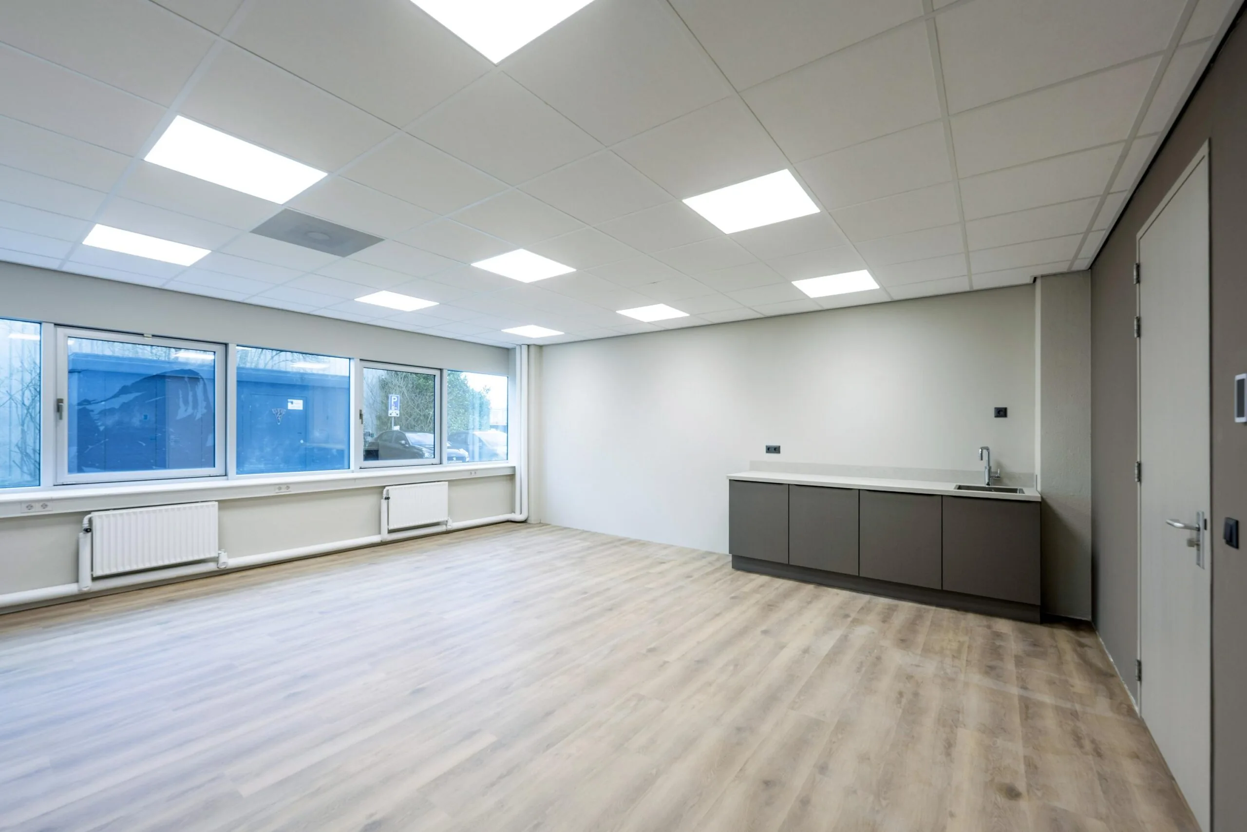 Lege kantoorruimte met grote ramen, plafondverlichting en een kitchenette aan de Kuiperbergweg.