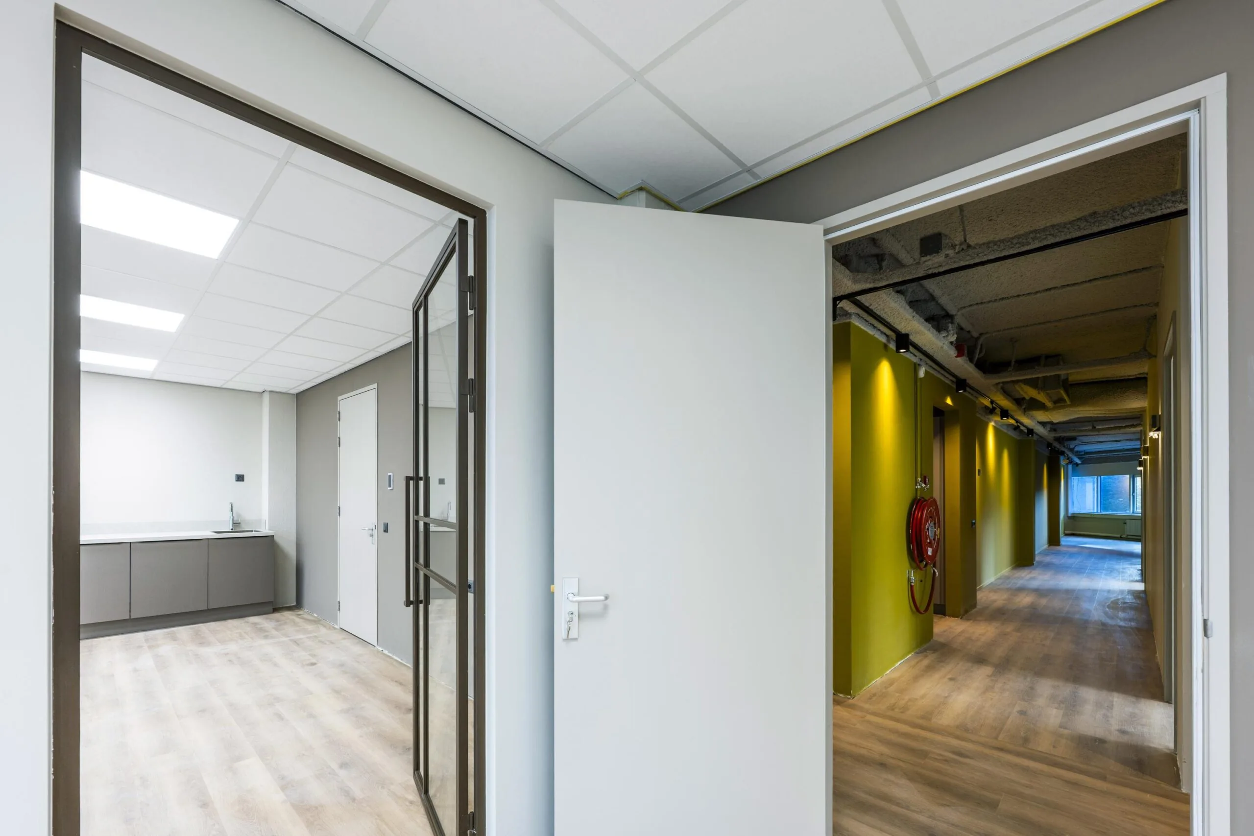 Een moderne kantoorruimte met een open deur, zichtbaar naar een gang met gele muren.