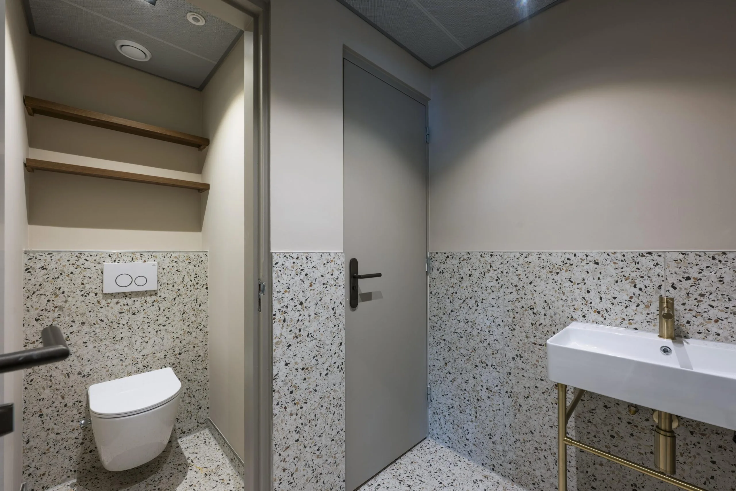 Een moderne badkamer met terrazzo wandtegels, een toilet, en een wastafel.