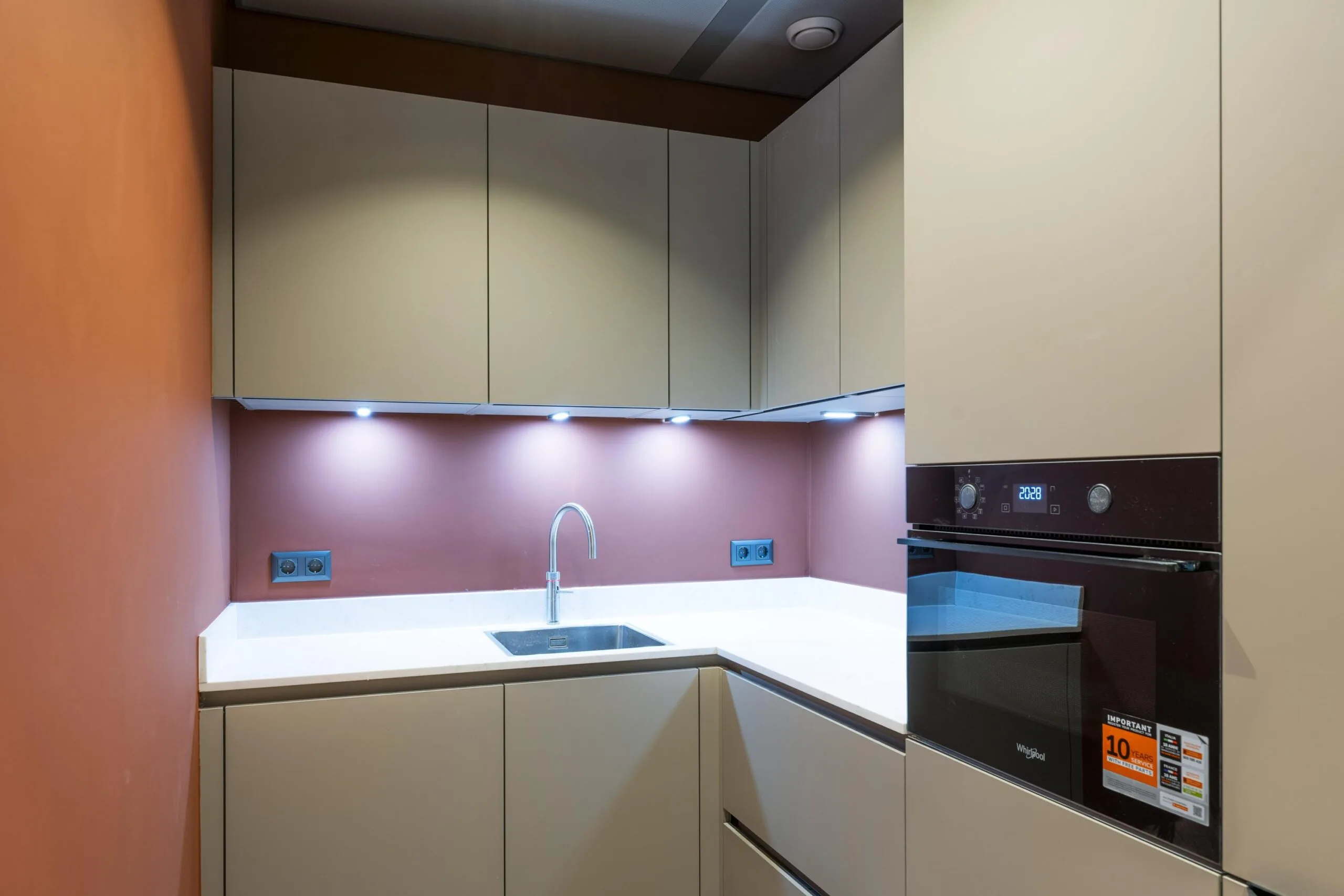 Een moderne keuken met beige kasten, een ingebouwde oven en een roestvrijstalen kraan boven een witte gootsteen.