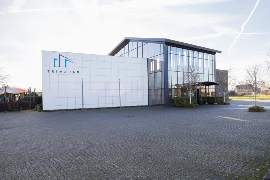 Een modern gebouw met een glazen gevel en het logo van Trimaran.