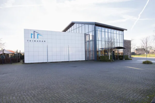 Een modern gebouw met een glazen gevel en het logo van Trimaran.