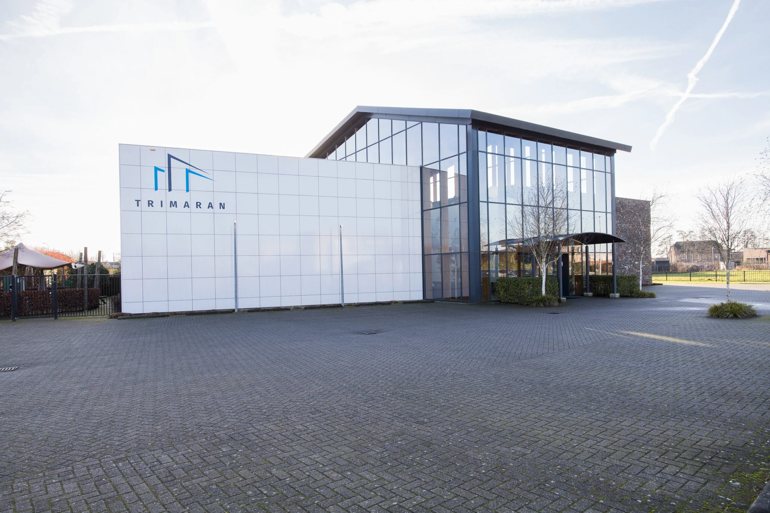 Een modern gebouw met een glazen gevel en het logo van Trimaran.