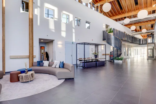 Een moderne lobby met een gebogen bank, planten, en een wenteltrap.