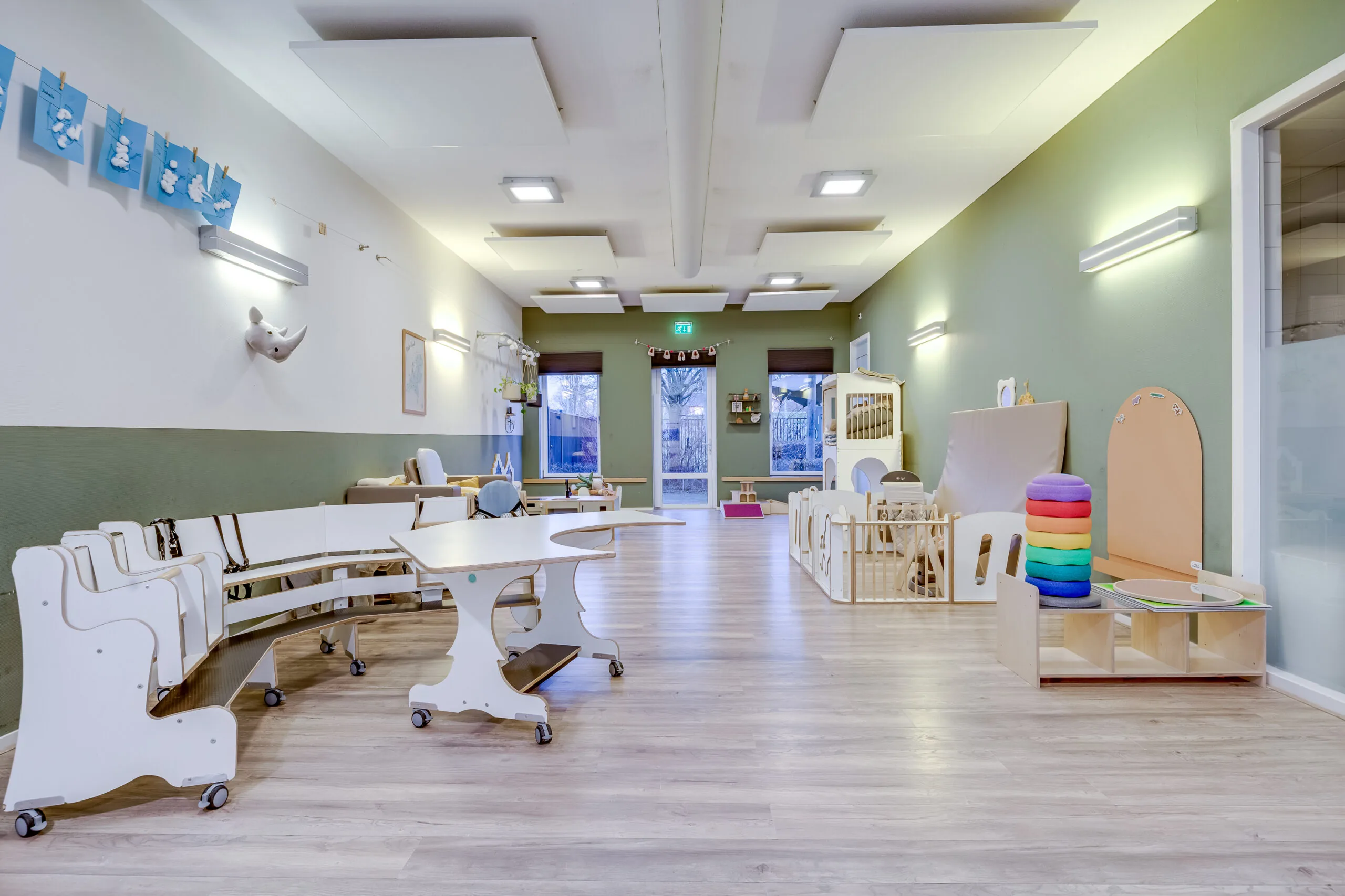 Een lichte, moderne kinderopvangruimte met houten meubels en speelobjecten.