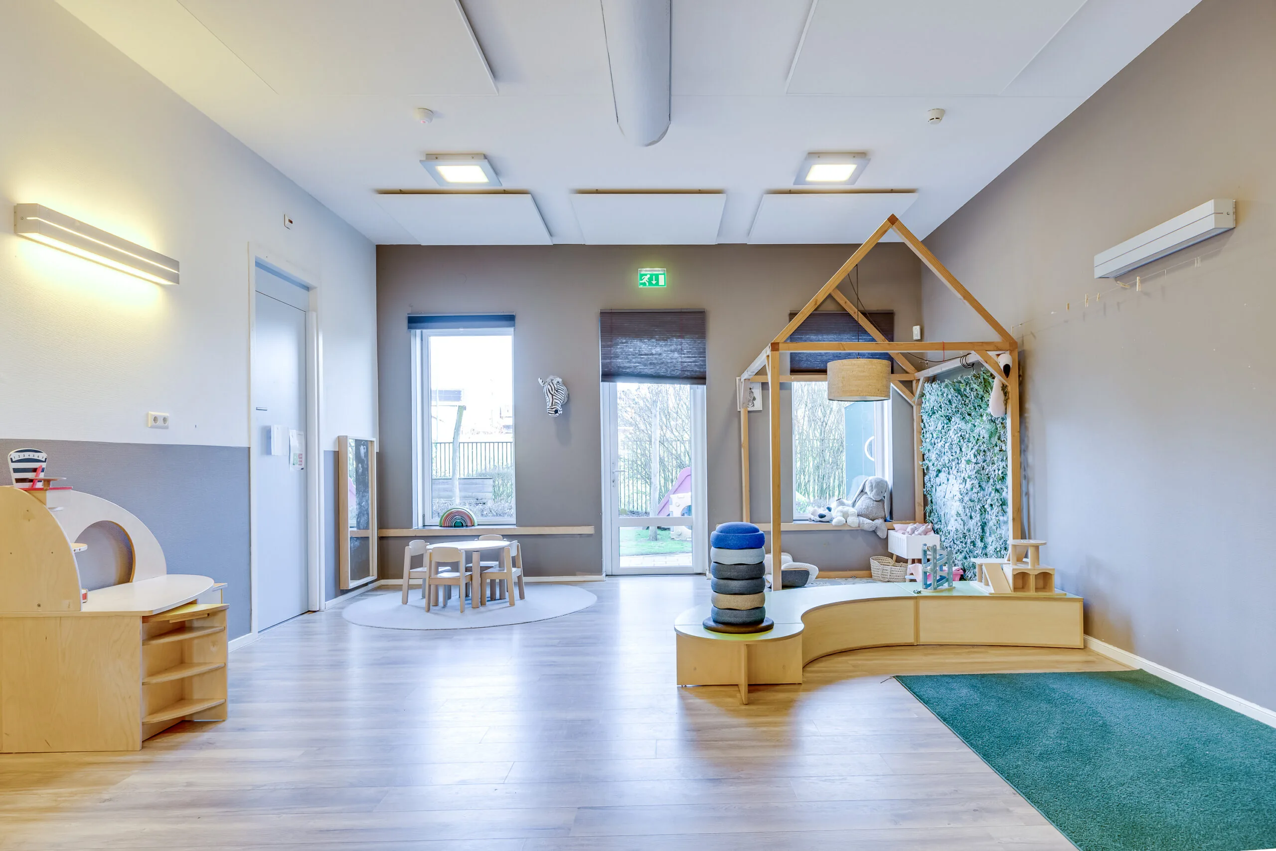 Een moderne, lichte kinderopvangruimte met houten meubels en speelgedeelten.
