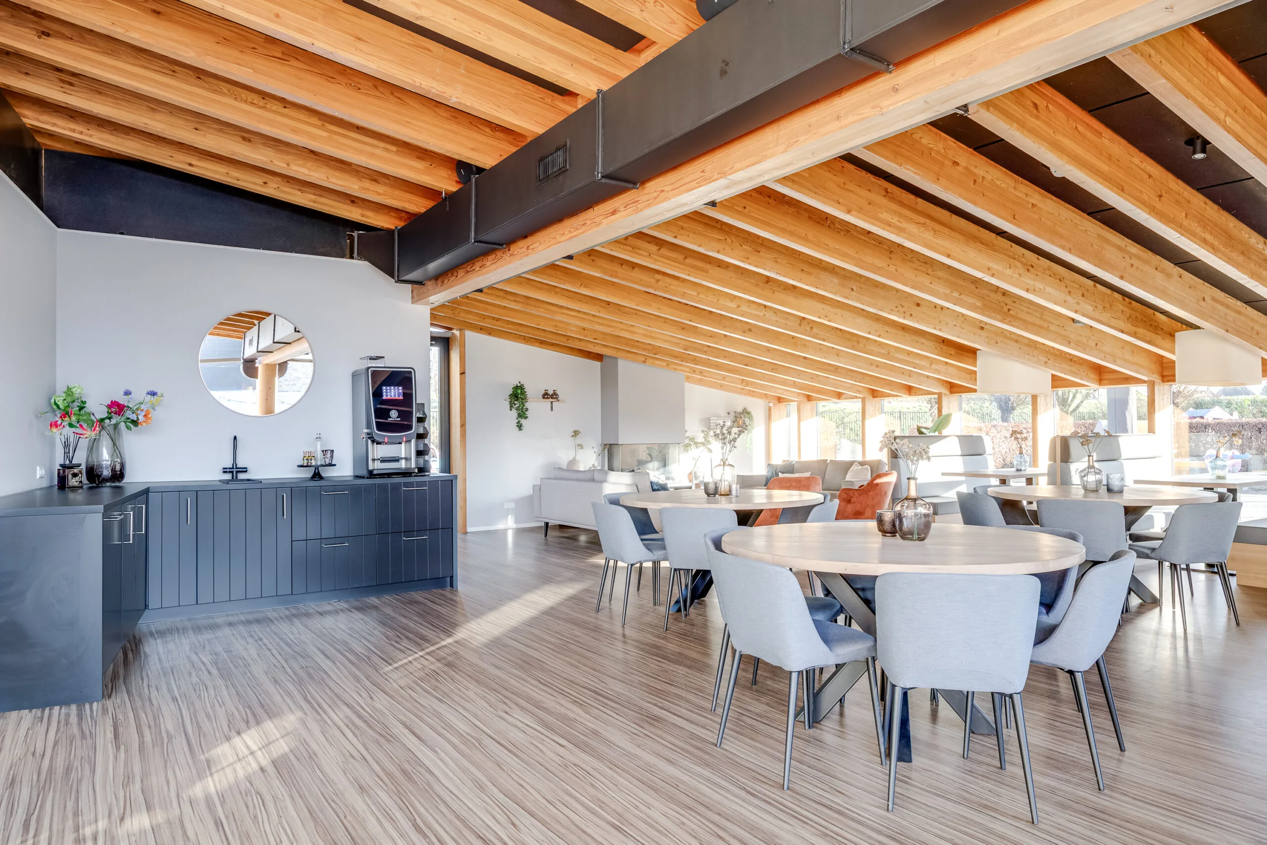 Een moderne, lichte ruimte met houten balken en een zithoek met ronde tafels en comfortabele stoelen.