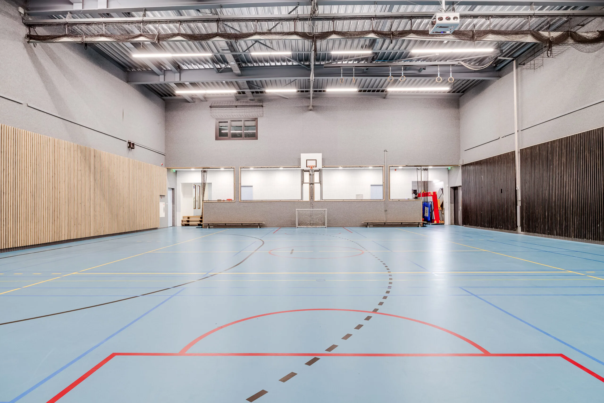 Een lege sporthal met blauwe vloer en basketbalnet.