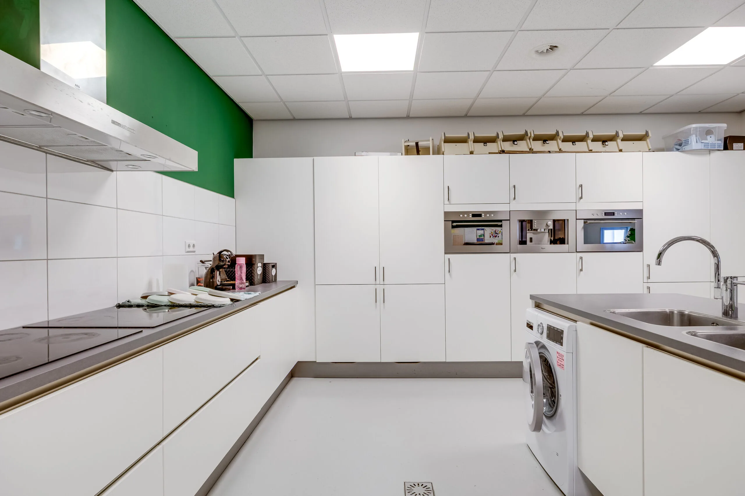 Moderne keuken met witte kasten, groene muur en ingebouwde apparaten.