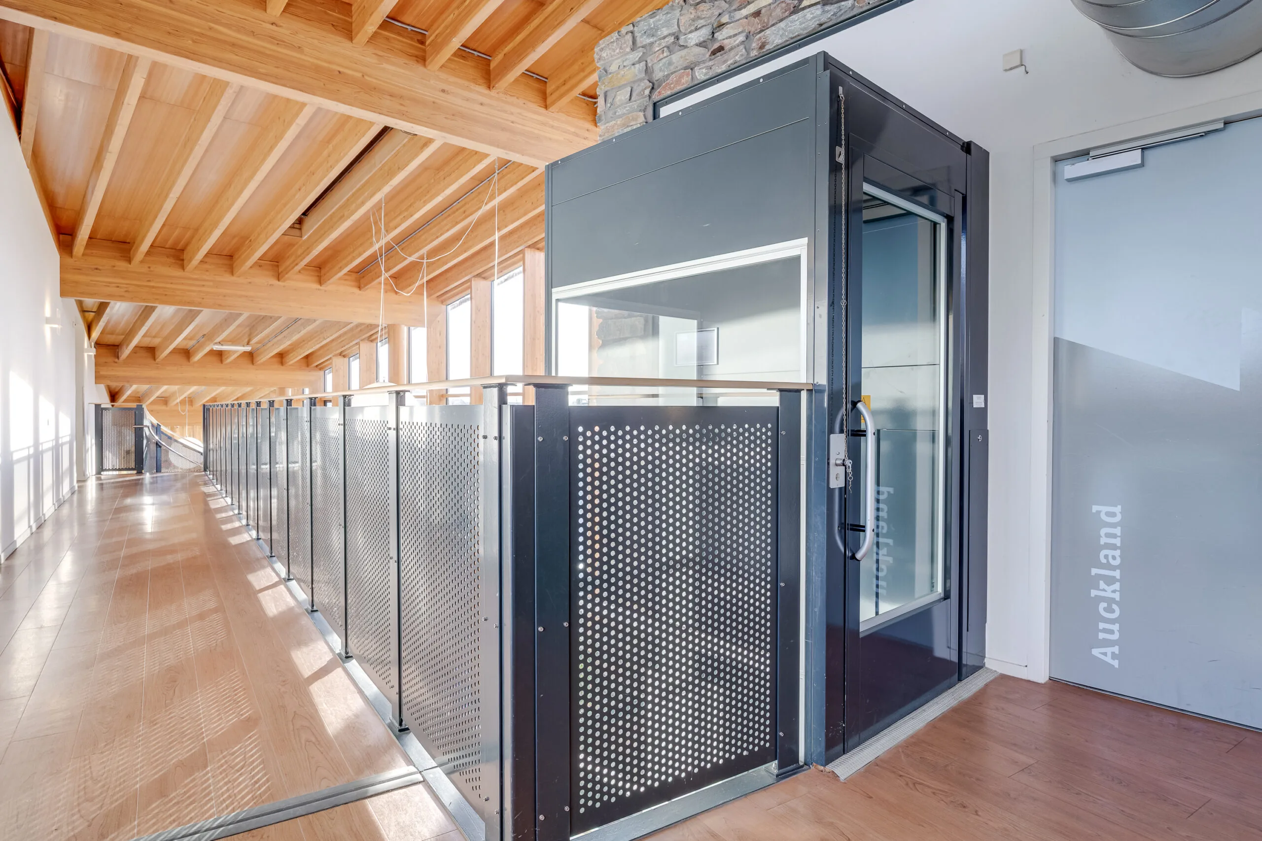 Een moderne corridor met houten plafond en glazen liftdeur met de tekst "Auckland".