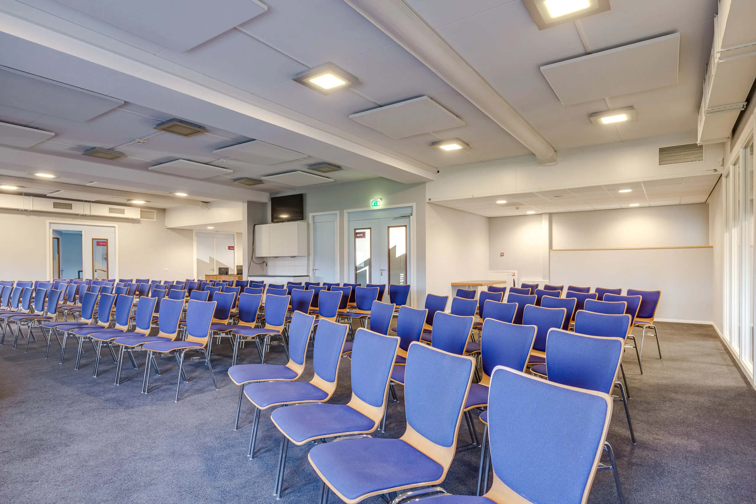 Een lege conferentiezaal met blauwe stoelen in keurige rijen opgesteld.