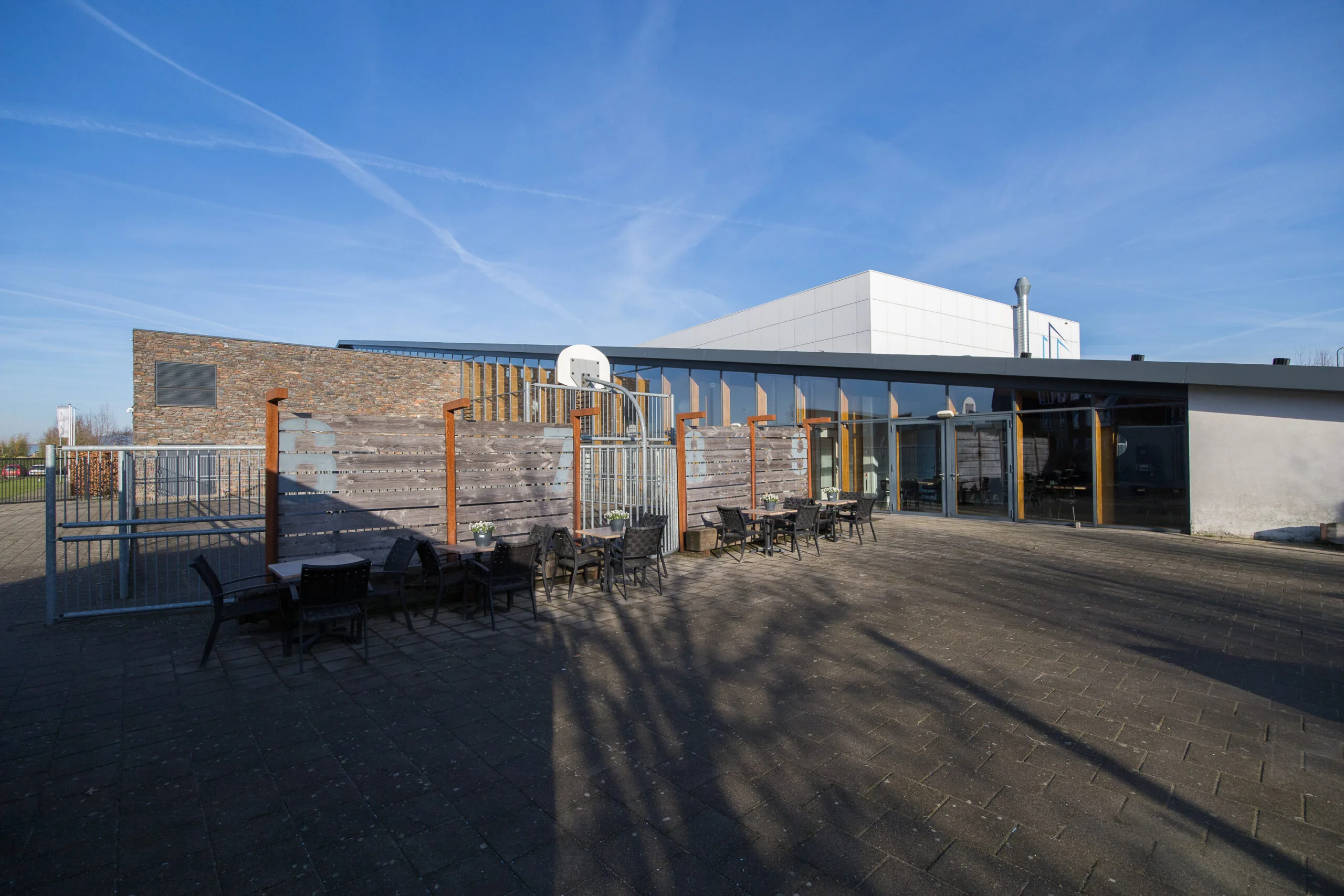 Een moderne buitenruimte met tafels en stoelen voor een gebouw onder een heldere blauwe lucht.