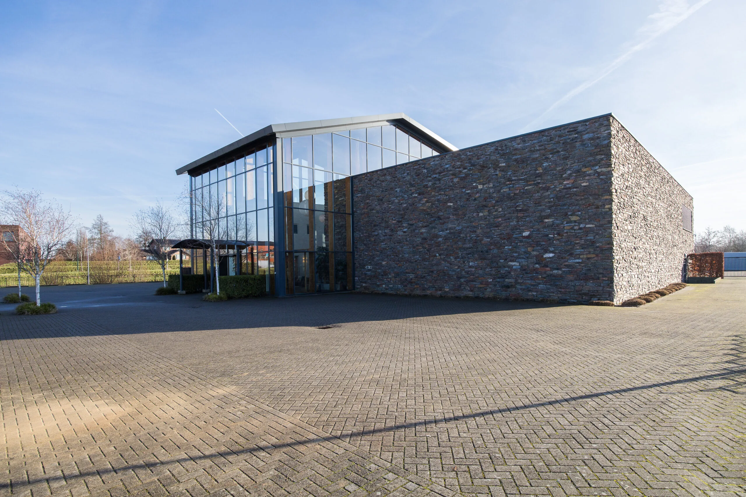 Een modern gebouw met grote glazen ramen en een stenen muur op een zonnige dag.