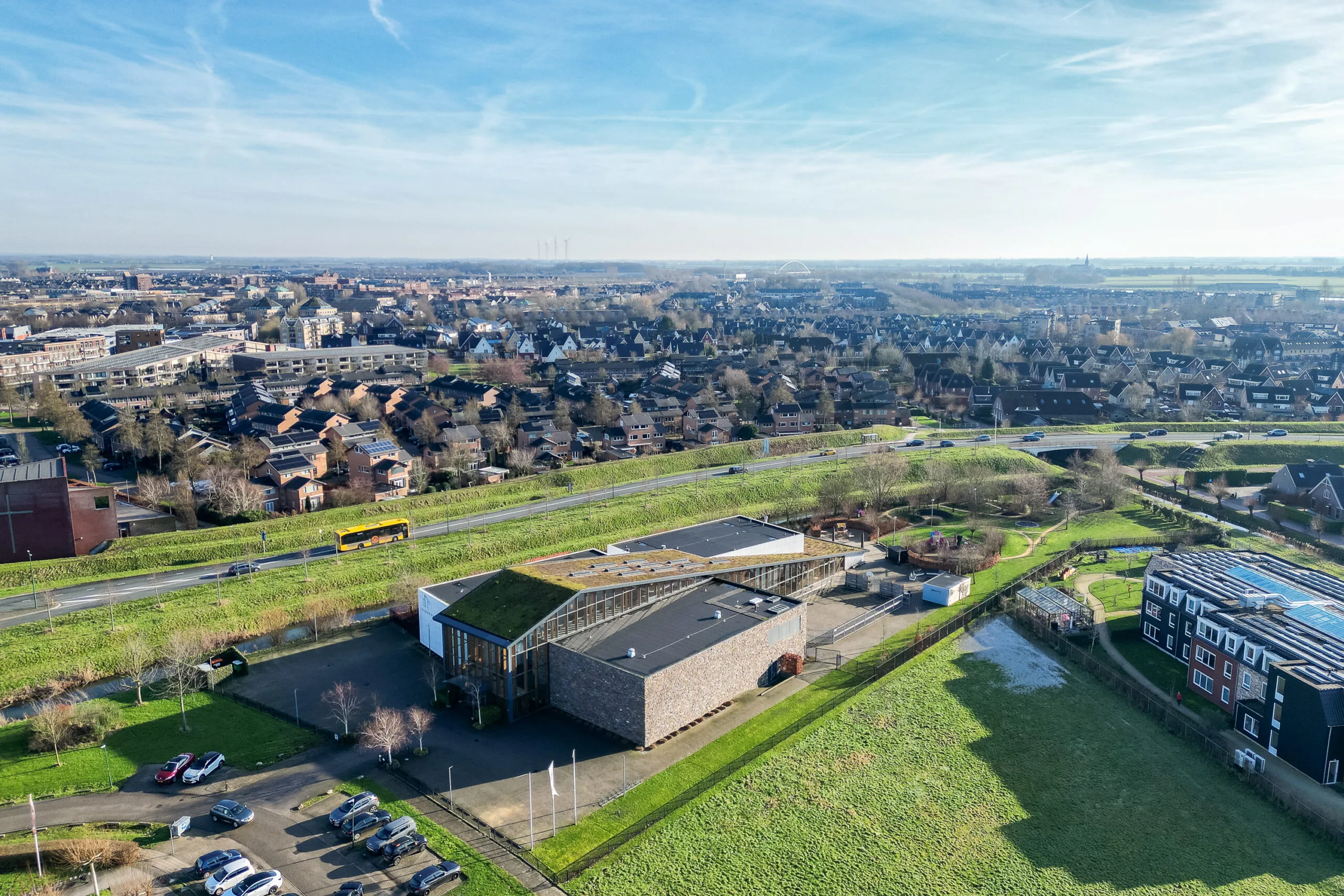 Luchtfoto van een stad met een modern gebouw met groen dak en omliggende wegen en huizen.