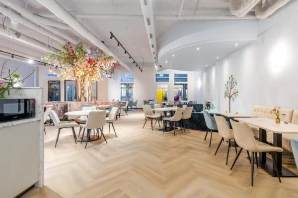 Een moderne, lichte eetruimte met tafels en stoelen, een decoratieve boom en grote ramen.