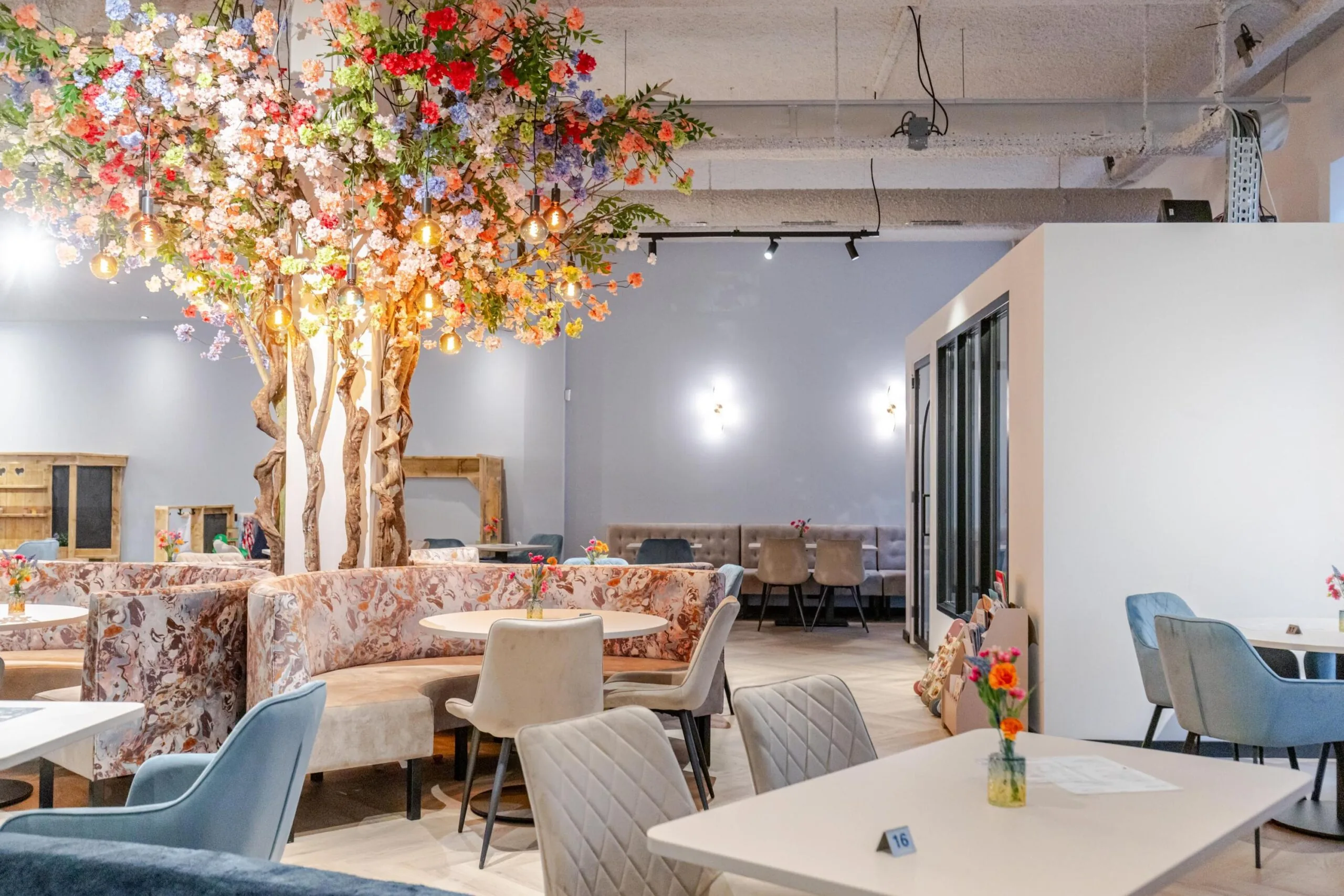Een sfeervol ingericht café met kleurrijke bloemenbomen en moderne zitplaatsen.