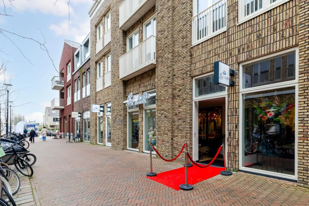 Een straatbeeld van de Westersingel met winkels en een rode loper bij een ingang.