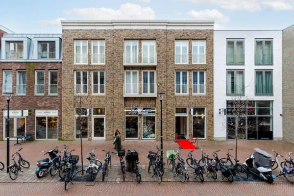 Een straatbeeld met een modern stenen gebouw aan de Westersingel, omgeven door geparkeerde fietsen en een voorbijganger.