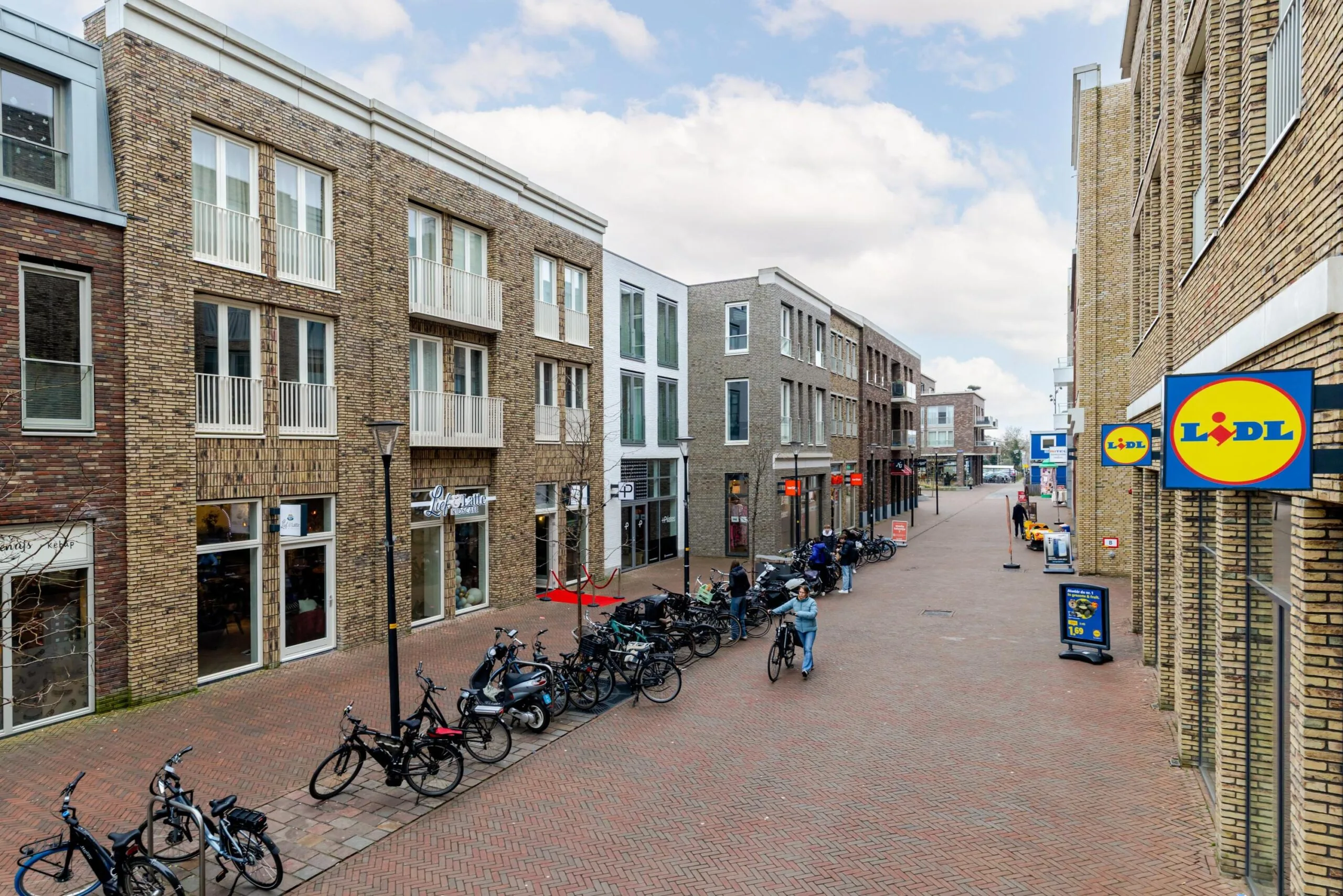 Straatbeeld met moderne bakstenen gebouwen, fietsen en een Lidl winkel aan de rechterkant.