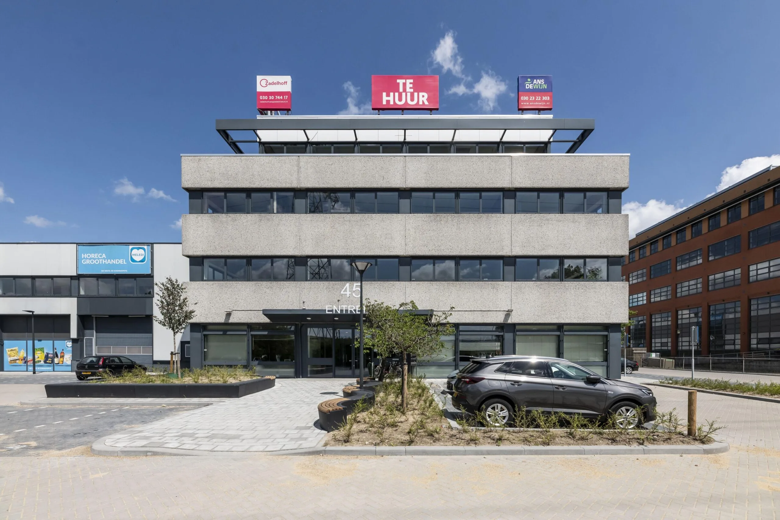 Kantoorgebouw met "Te Huur" borden op het dak en geparkeerde auto's ervoor.
