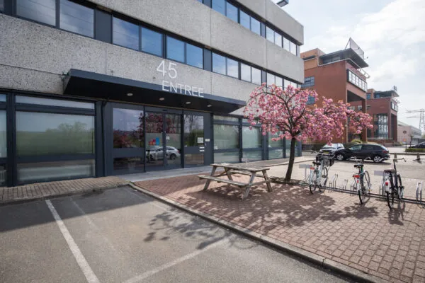 Vooraanzicht van het gebouw "45 Entree" met een bloeiende boom en fietsenrekken op de voorgrond.